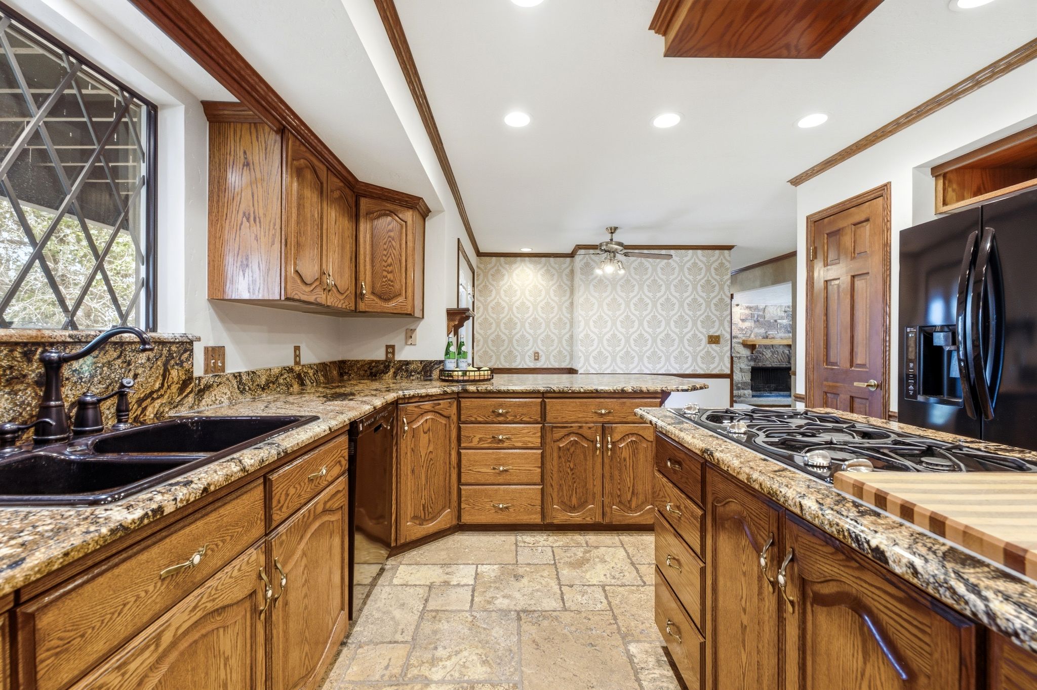 Kitchen featuring wood cabinetry, granite countertops, a black double-basin sink with an oil-rubbed bronze faucet, a gas cooktop, and a black refrigerator
