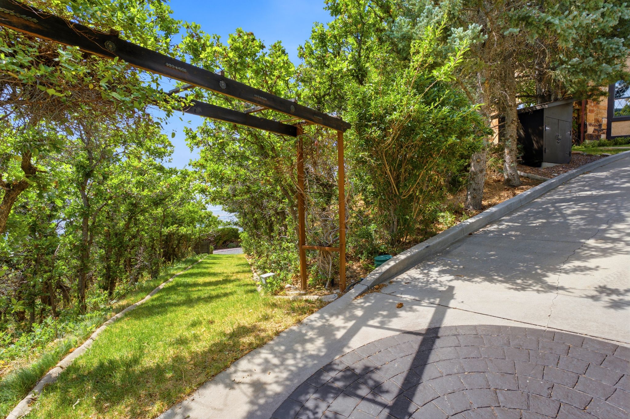 Landscaped pathways entrance featuring a rustic wooden arbor, verdant foliage, and a manicured lawn