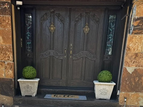Richly carved double entry doors with decorative hardware and side lights featuring patterned glass