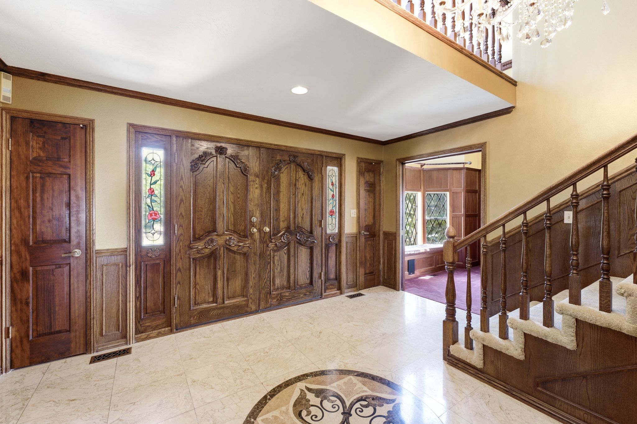 Grand entryway featuring ornate double doors, decorative sidelights, and a marble-finish tile floor with a medallion inlay