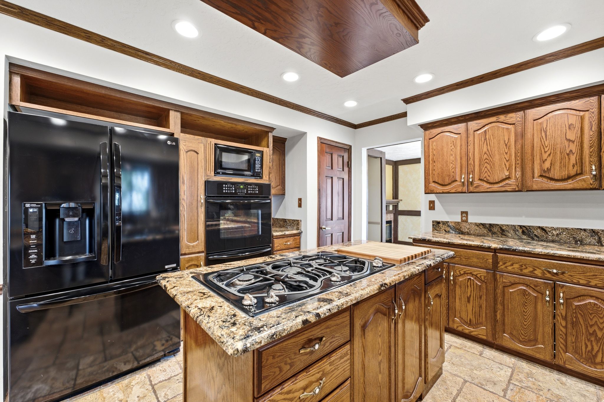 Kitchen featuring an island with a built-in gas cooktop, granite countertops, wood cabinetry, black appliances, and recessed lighting