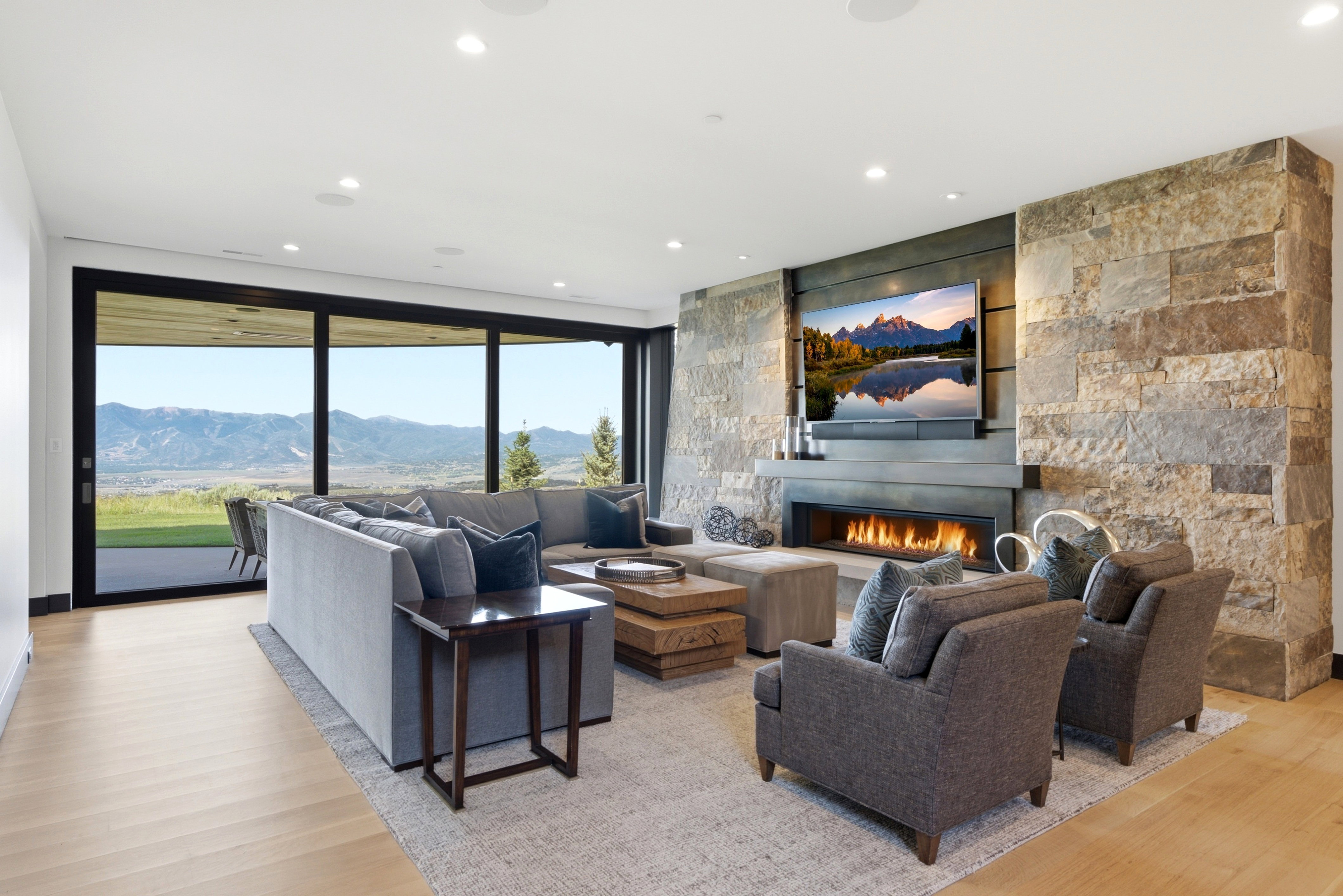 Spacious living area featuring a stone fireplace with a linear gas insert, large format sliding glass doors, light wood-finish flooring, recessed lighting, and integrated ceiling speakers