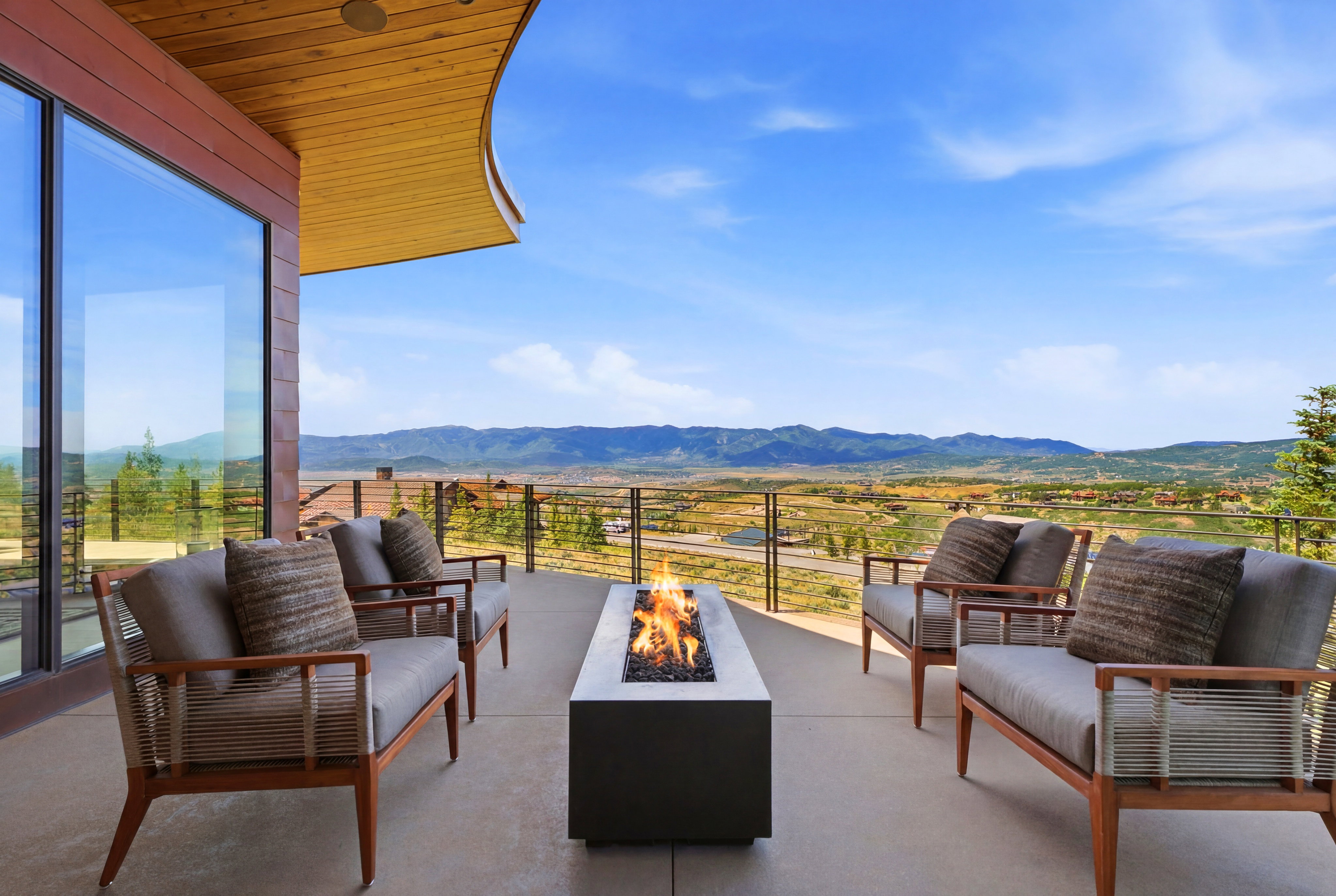 Expansive outdoor patio featuring a built-in fire pit, clear panel railing, and a wood-finish ceiling