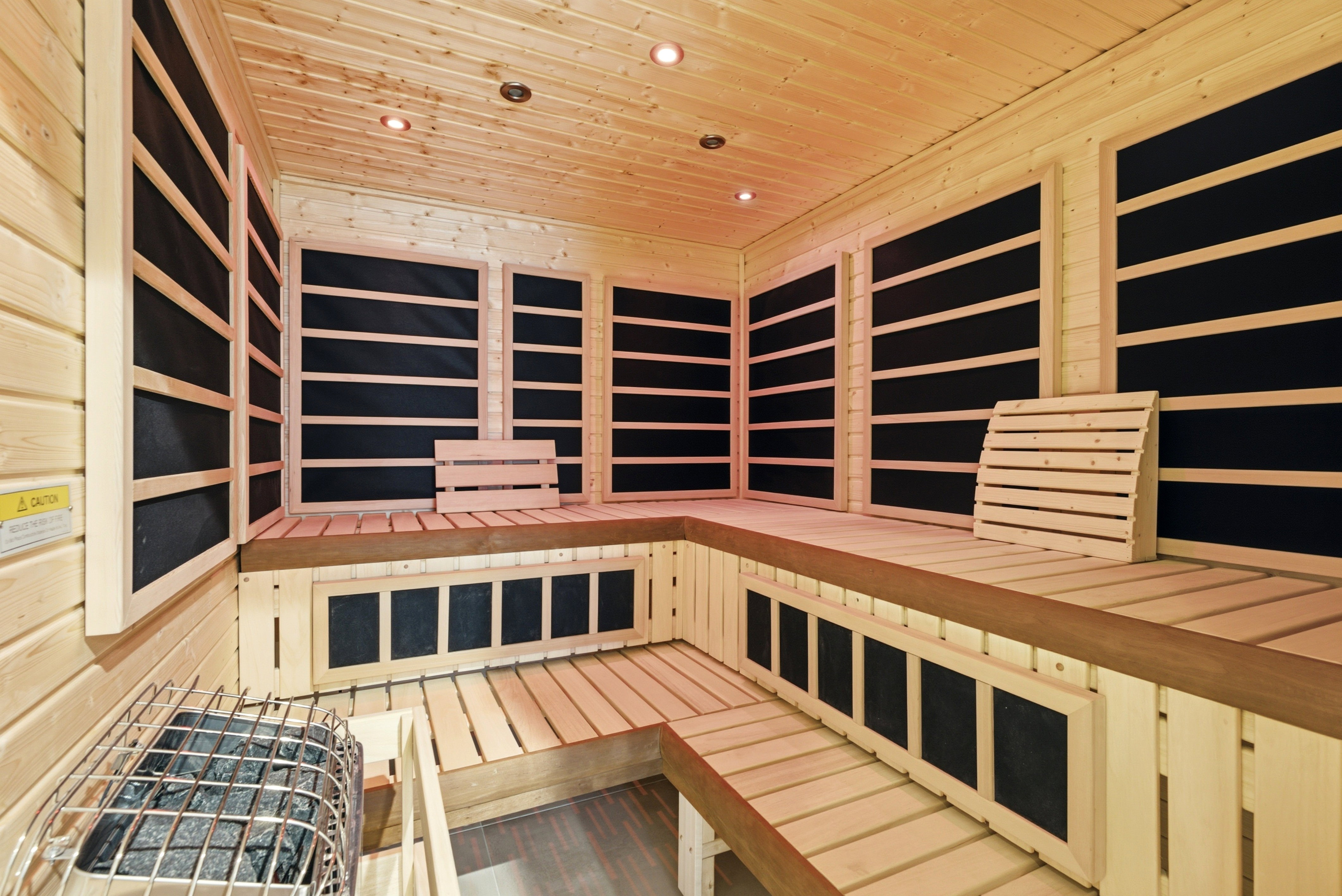 Custom-built cedar sauna featuring multiple-tiered bench seating, integrated heating panels, recessed ceiling lighting, and a floor-standing electric heater