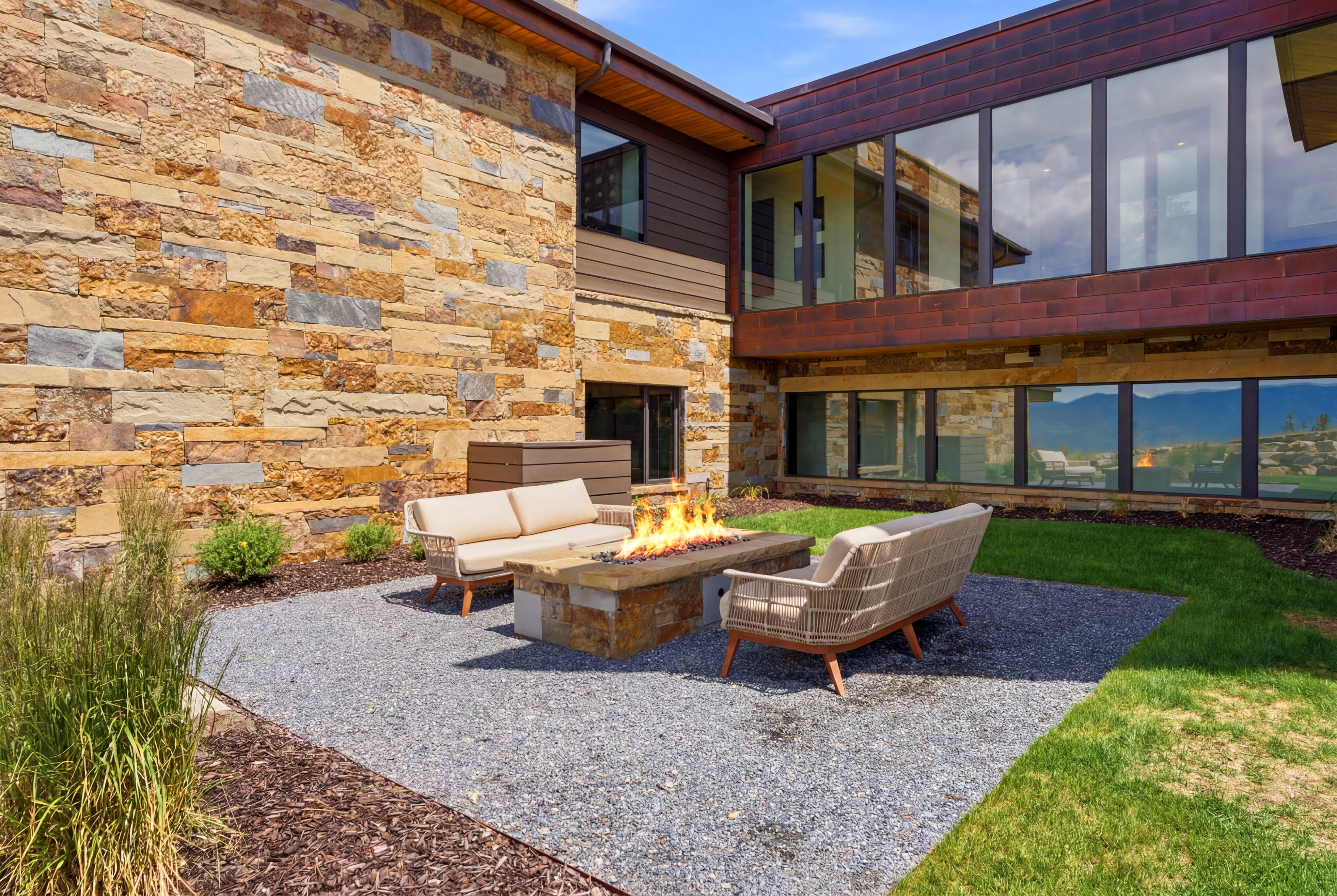 Exterior patio featuring a built-in stone fire pit, gravel flooring, and a stone-clad facade