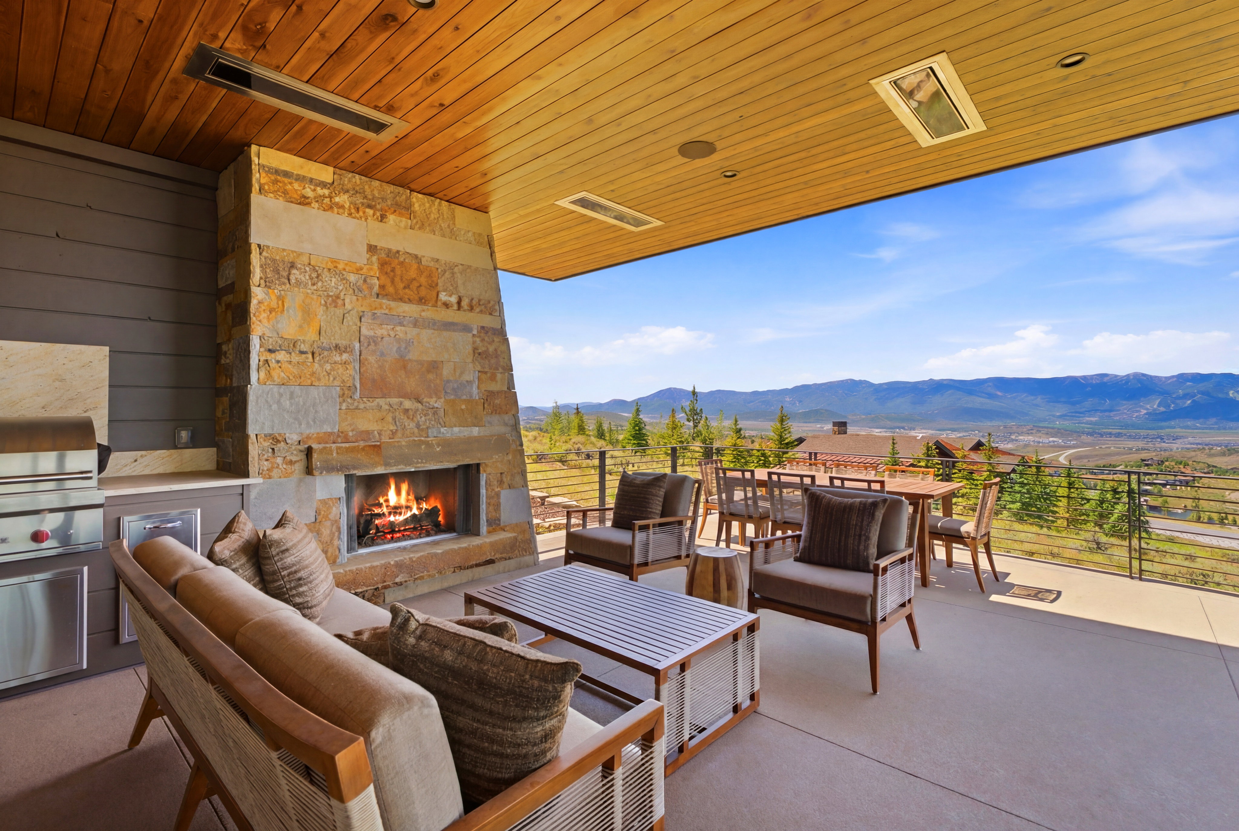 Expansive outdoor living area featuring a stone fireplace, built-in barbecue with stainless steel appliances, and a wood-paneled ceiling