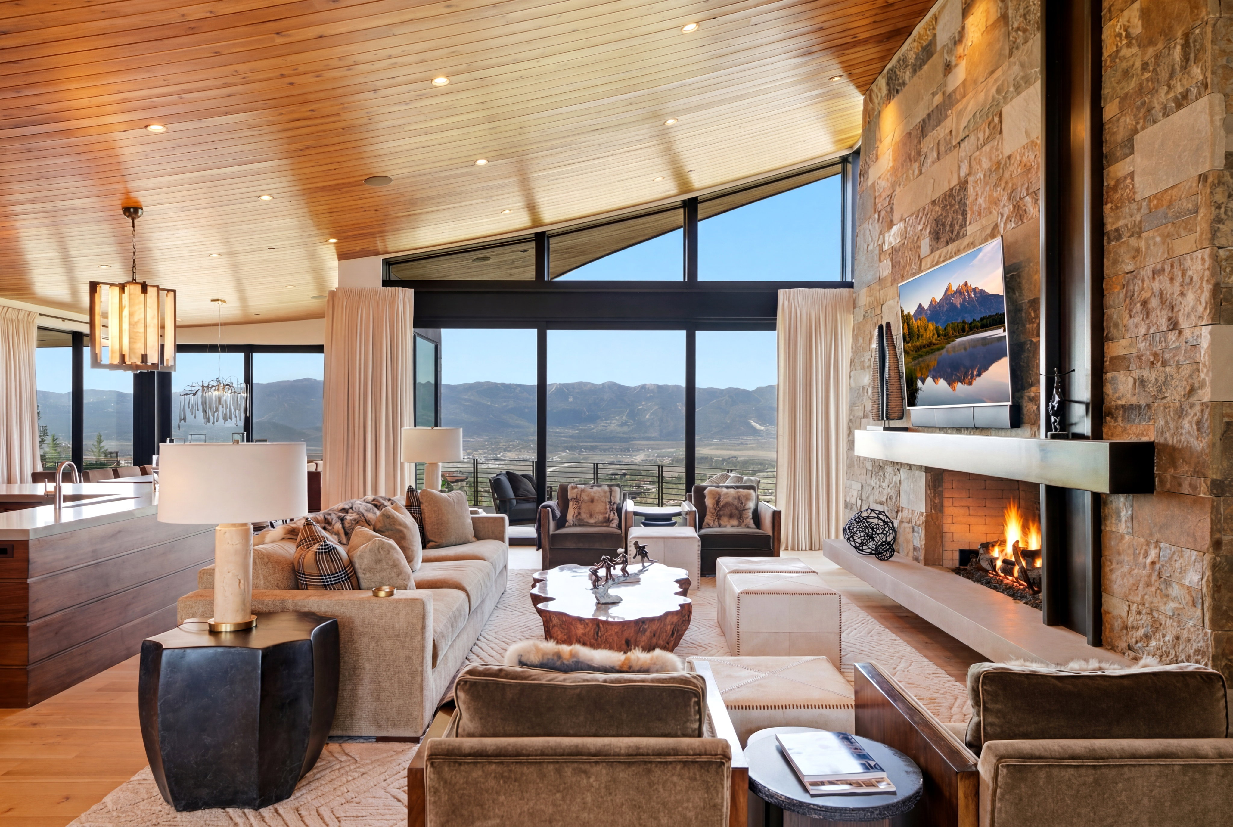 Open-concept living space featuring a stone-clad fireplace with a suspended hearth, a wood-paneled vaulted ceiling, and expansive floor-to-ceiling windows