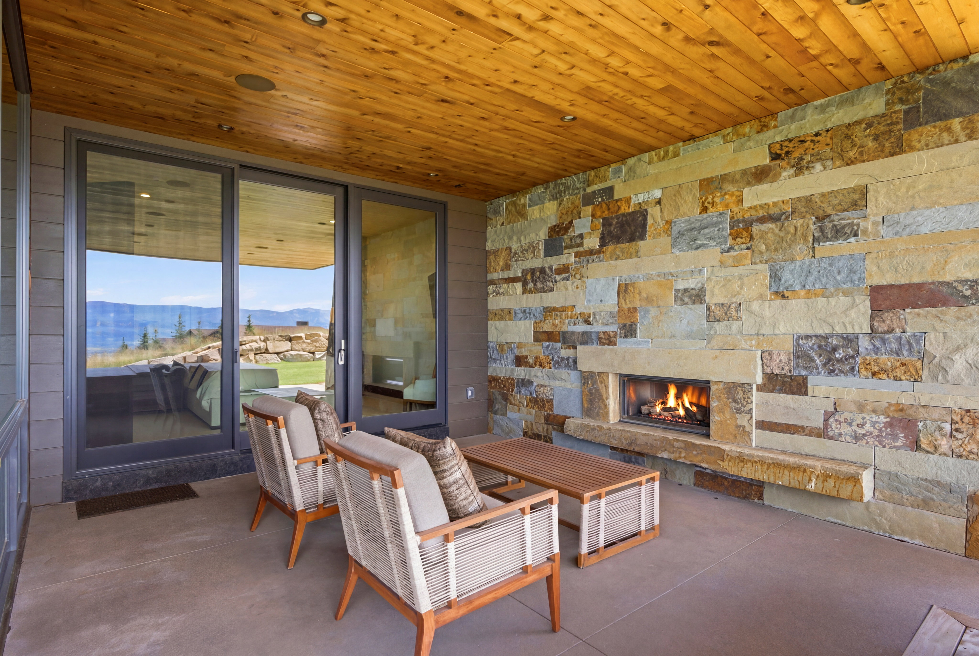Covered patio featuring a full-height stone wall with an integrated fireplace, wood-finish ceiling, and large sliding glass doors