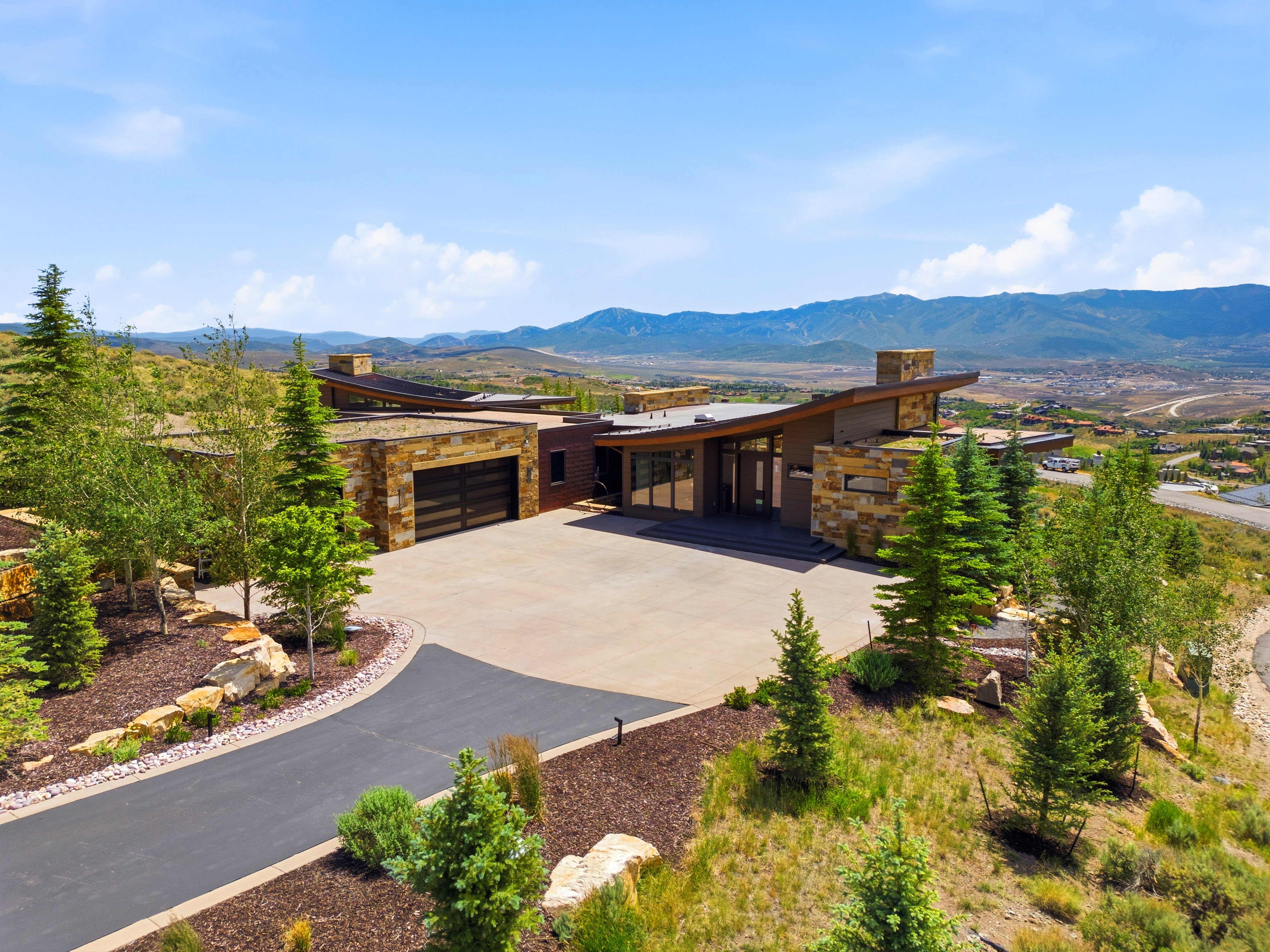 Contemporary residence featuring a multi-layered roofline, stone and wood-finish exterior accents, and a large concrete driveway