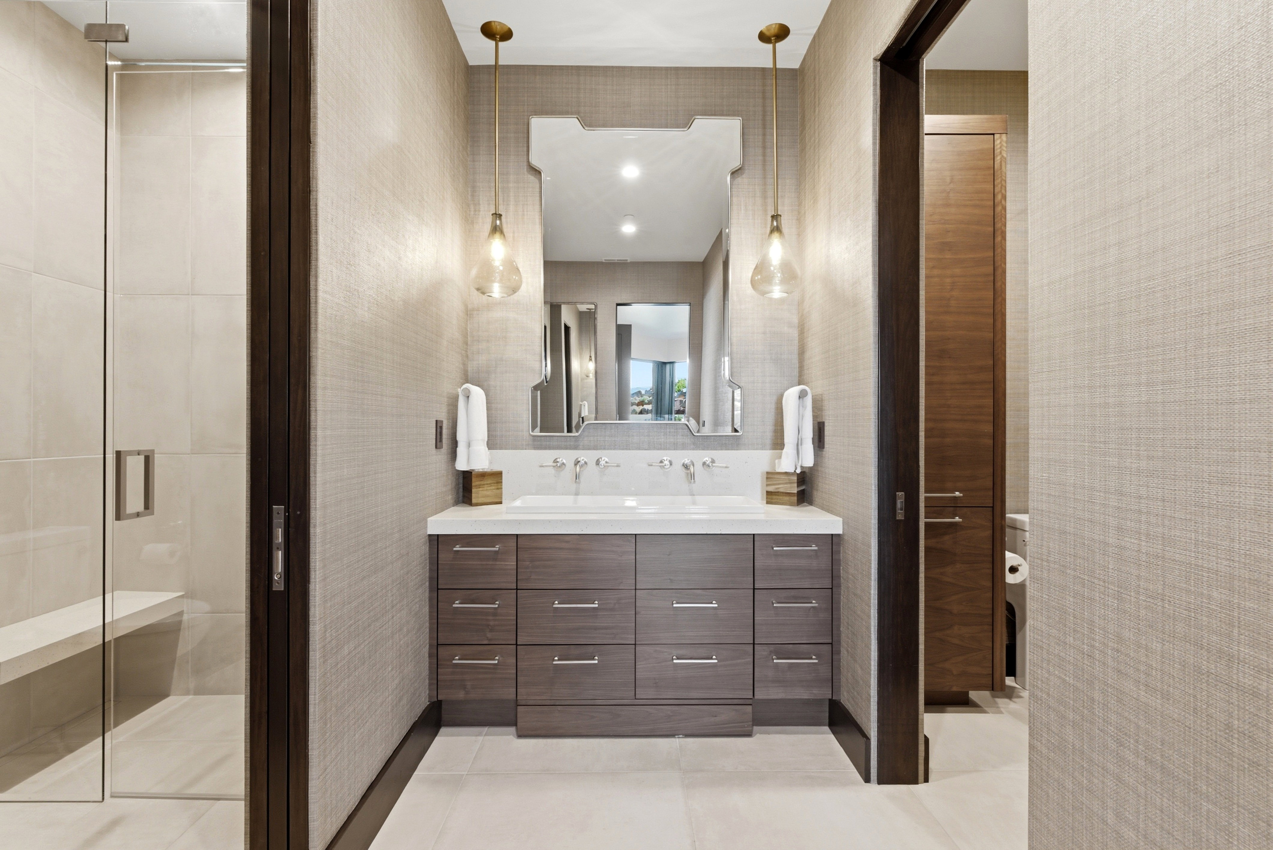 Contemporary bathroom featuring a double vanity with dark wood-finish cabinetry and a white countertop, two vessel sinks, and wall-mounted faucets