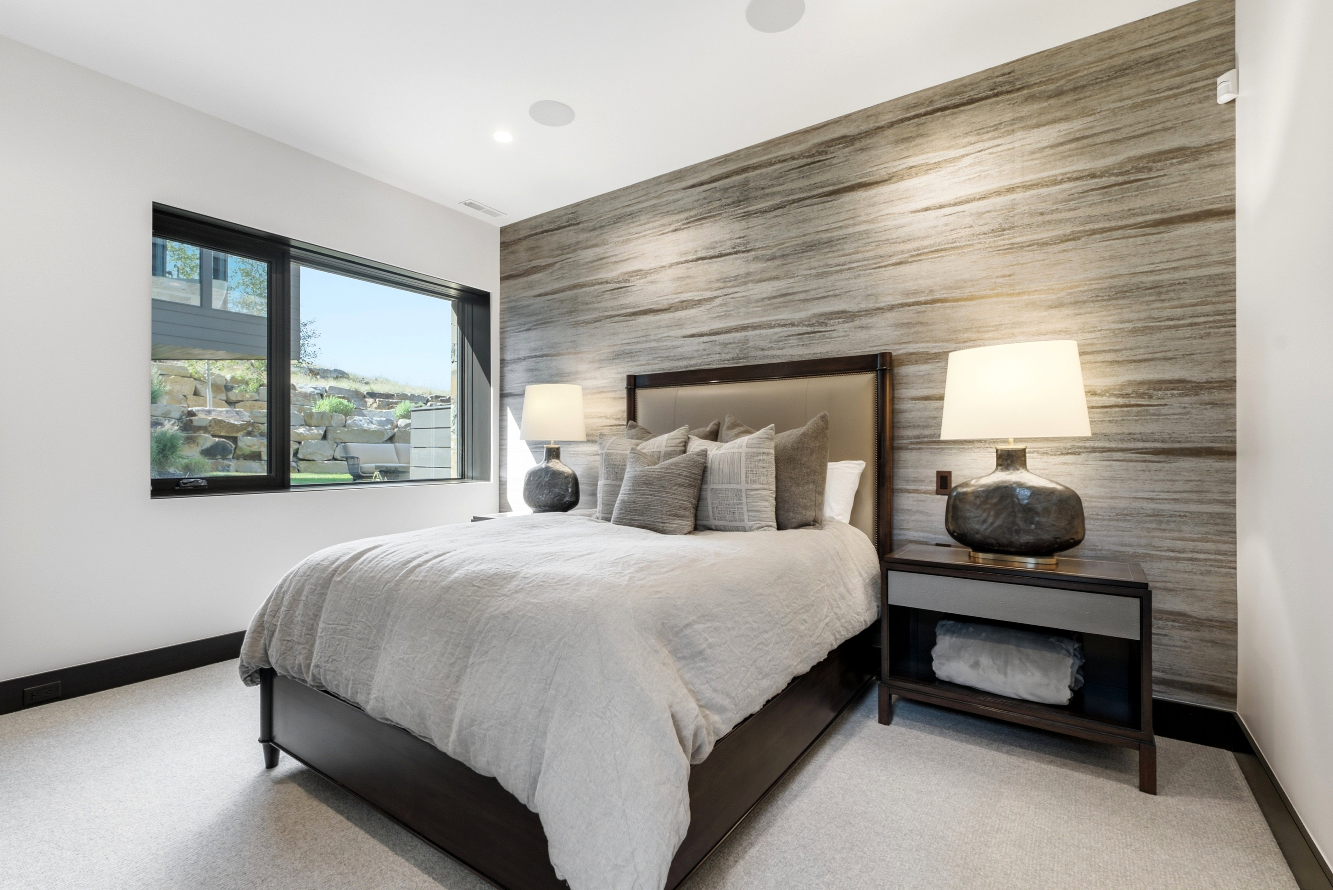 Bedroom featuring an accent wall with horizontal striations, a large window with black framing, recessed ceiling lighting, and light-toned carpeting