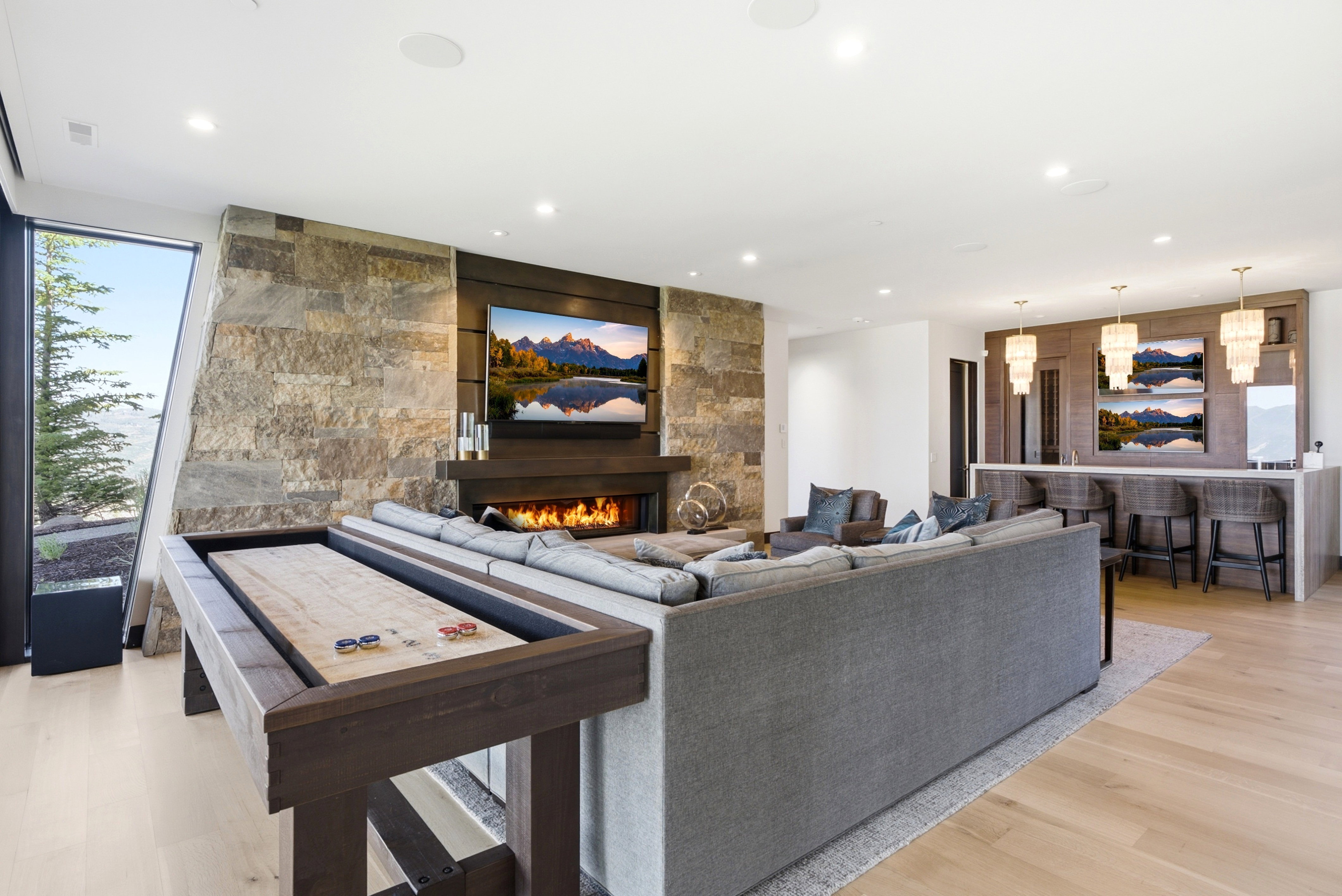 Spacious living area featuring a stacked stone fireplace surround, an integrated media center, and a wet bar with pendant lighting