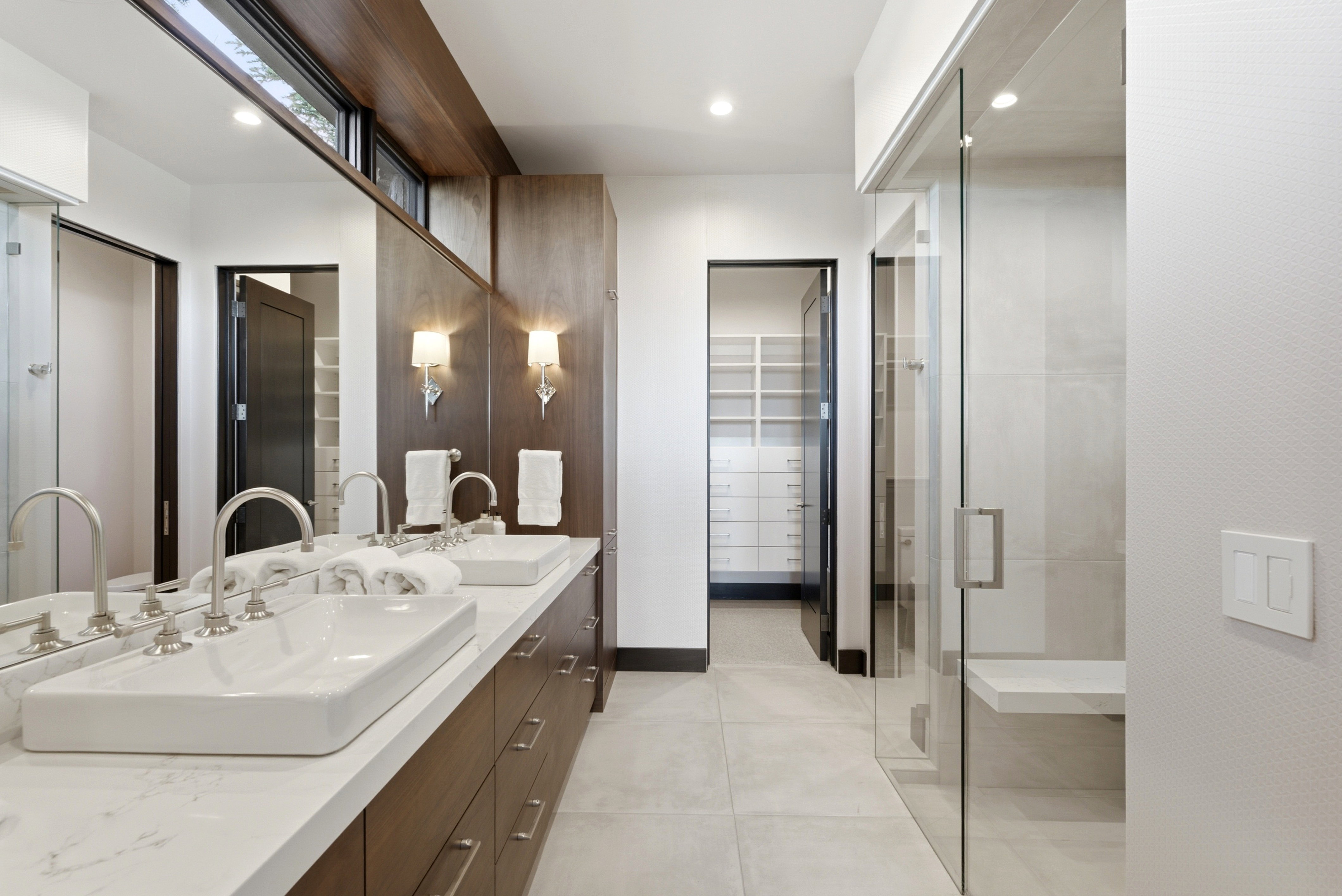 Contemporary bathroom featuring a dual vanity with rectangular vessel sinks, extensive wood-finish cabinetry, and a spacious glass-enclosed shower with a built-in bench