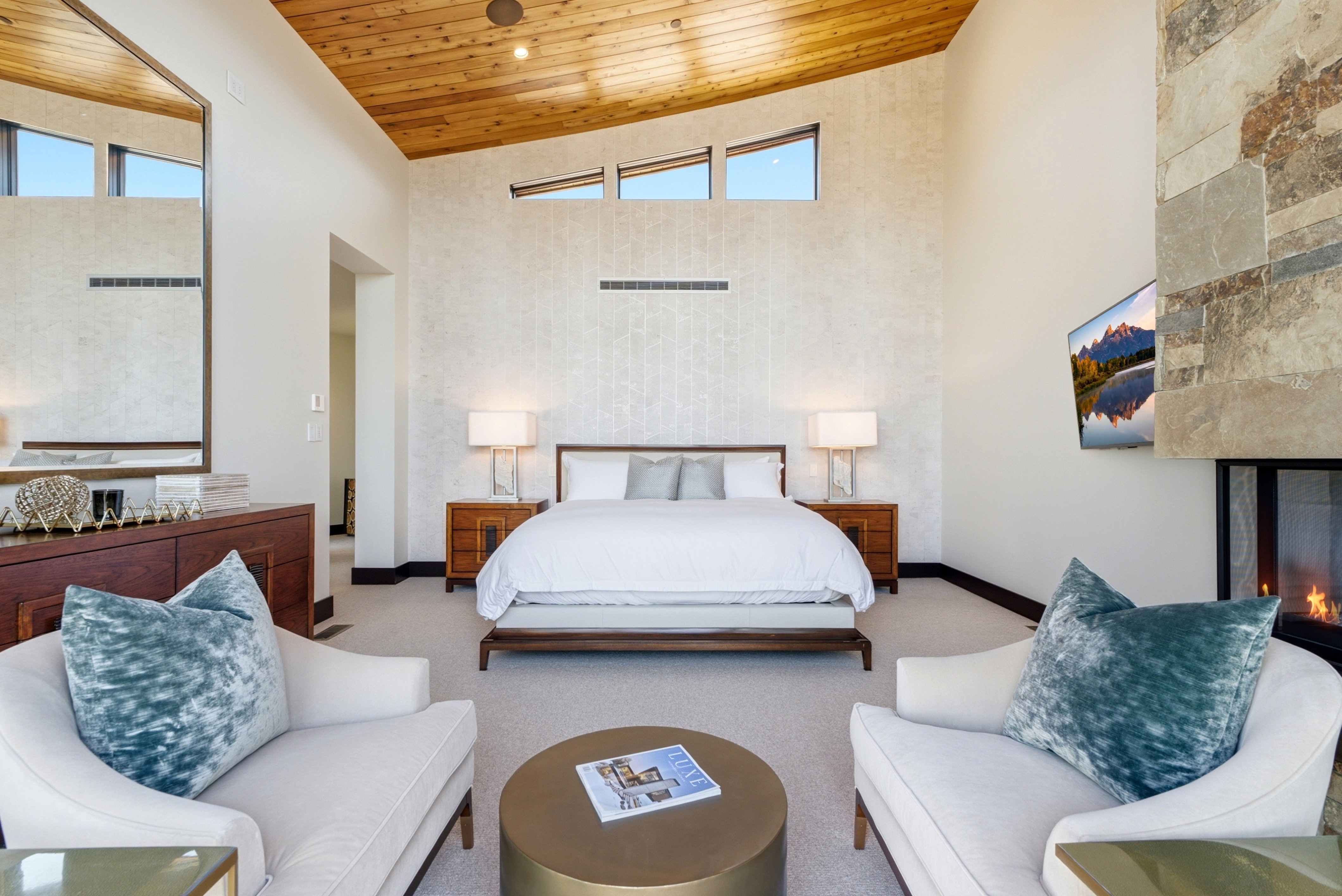 Spacious room featuring a vaulted wood-finish ceiling, a stone-clad fireplace with glass doors, and high transom windows
