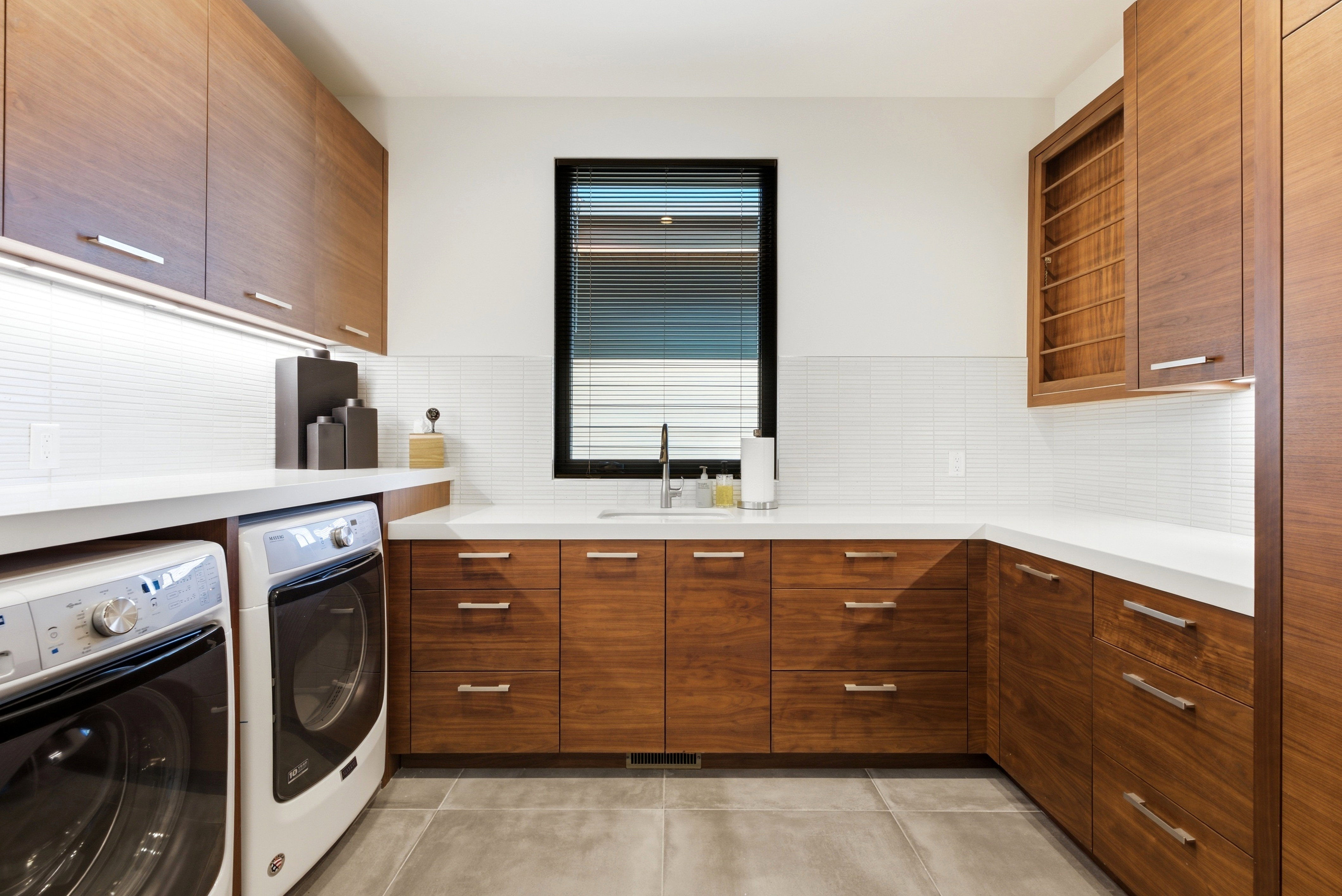 Contemporary utility room featuring extensive wood-finish cabinetry, white solid surface countertops, and a white tile backsplash