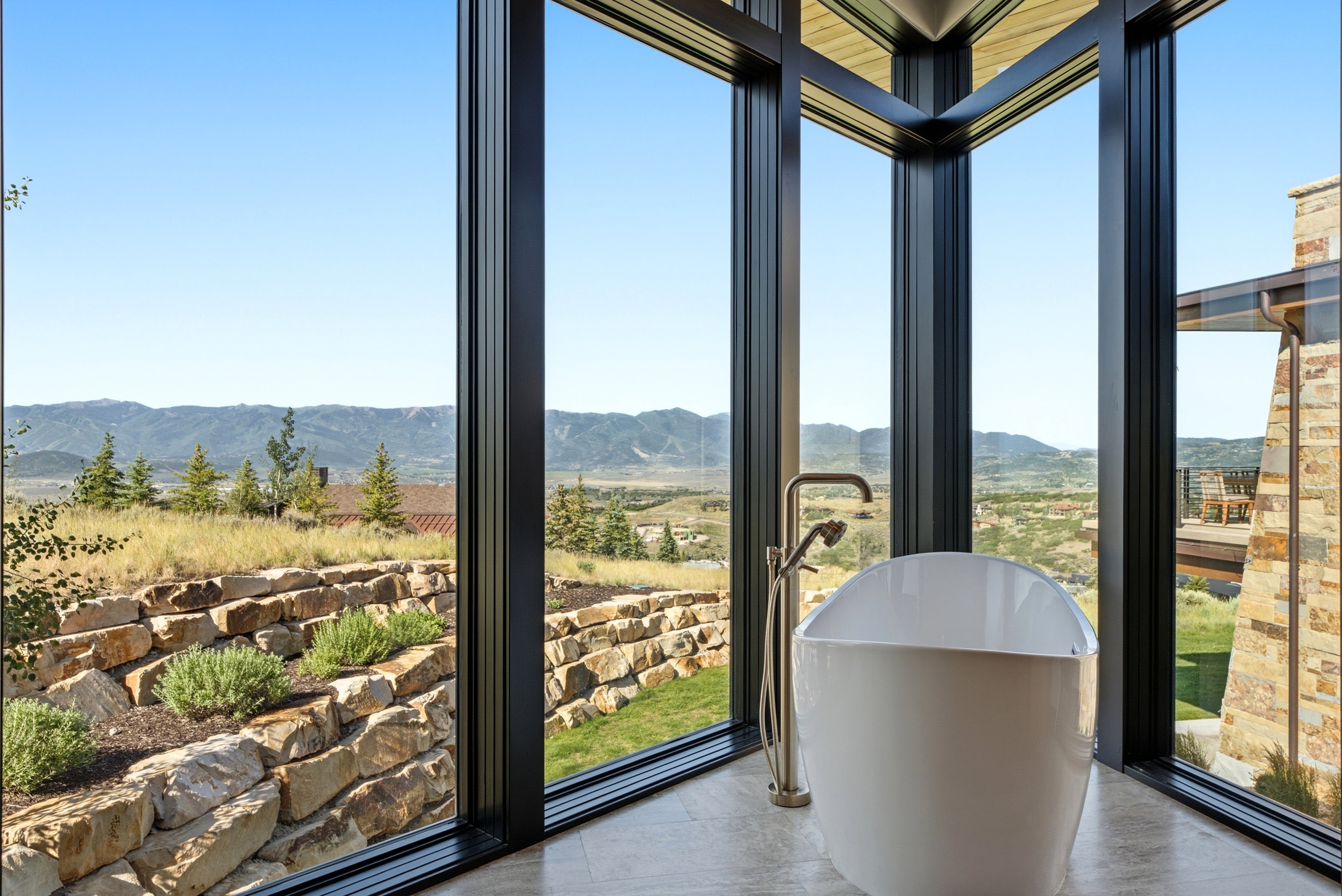 Contemporary soaking tub with a floor-mounted brushed nickel faucet, set against a backdrop of floor-to-ceiling windows