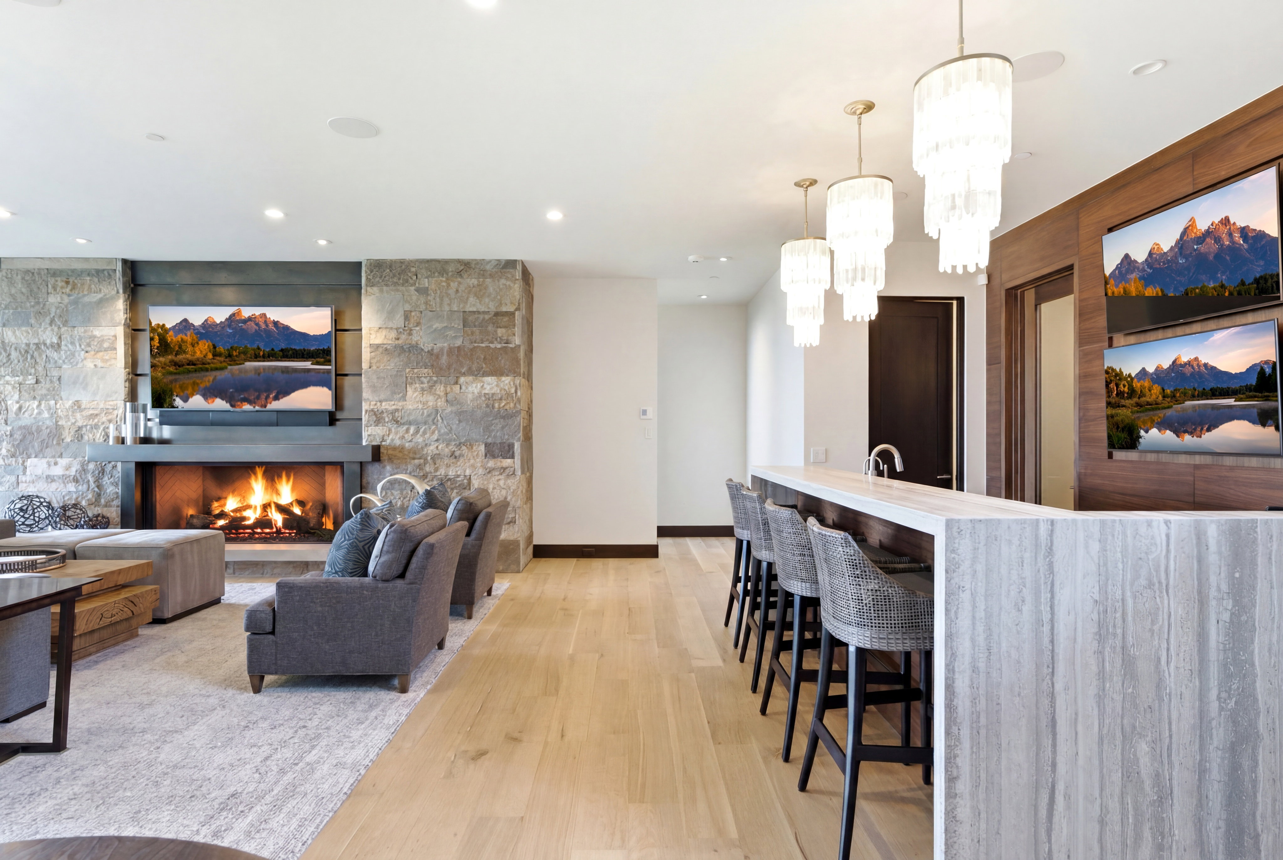 Spacious living area featuring a stone accent wall with a built-in fireplace, light wood-finish flooring, and a large wet bar with seating for four