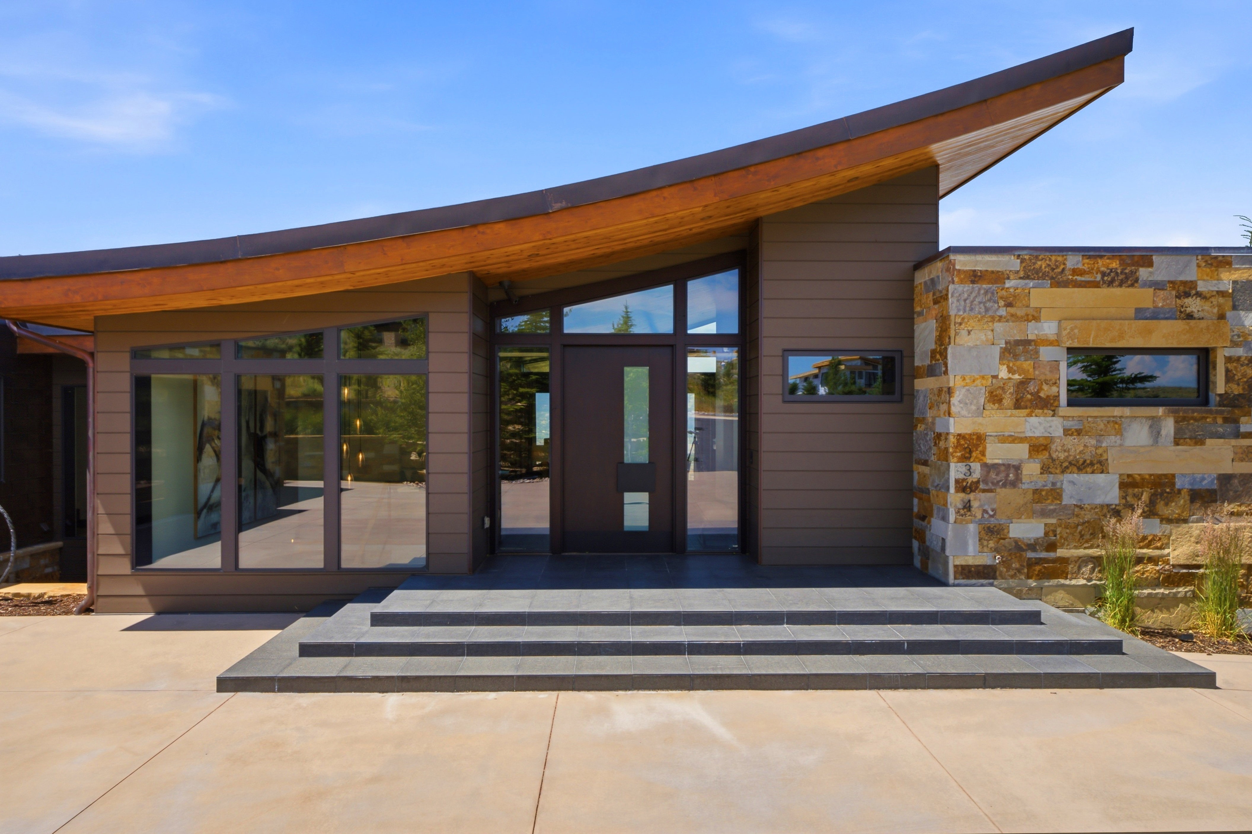 Modern architectural facade featuring a curved roofline with a wood soffit, stone veneer accent wall, and multiple floor-to-ceiling windows