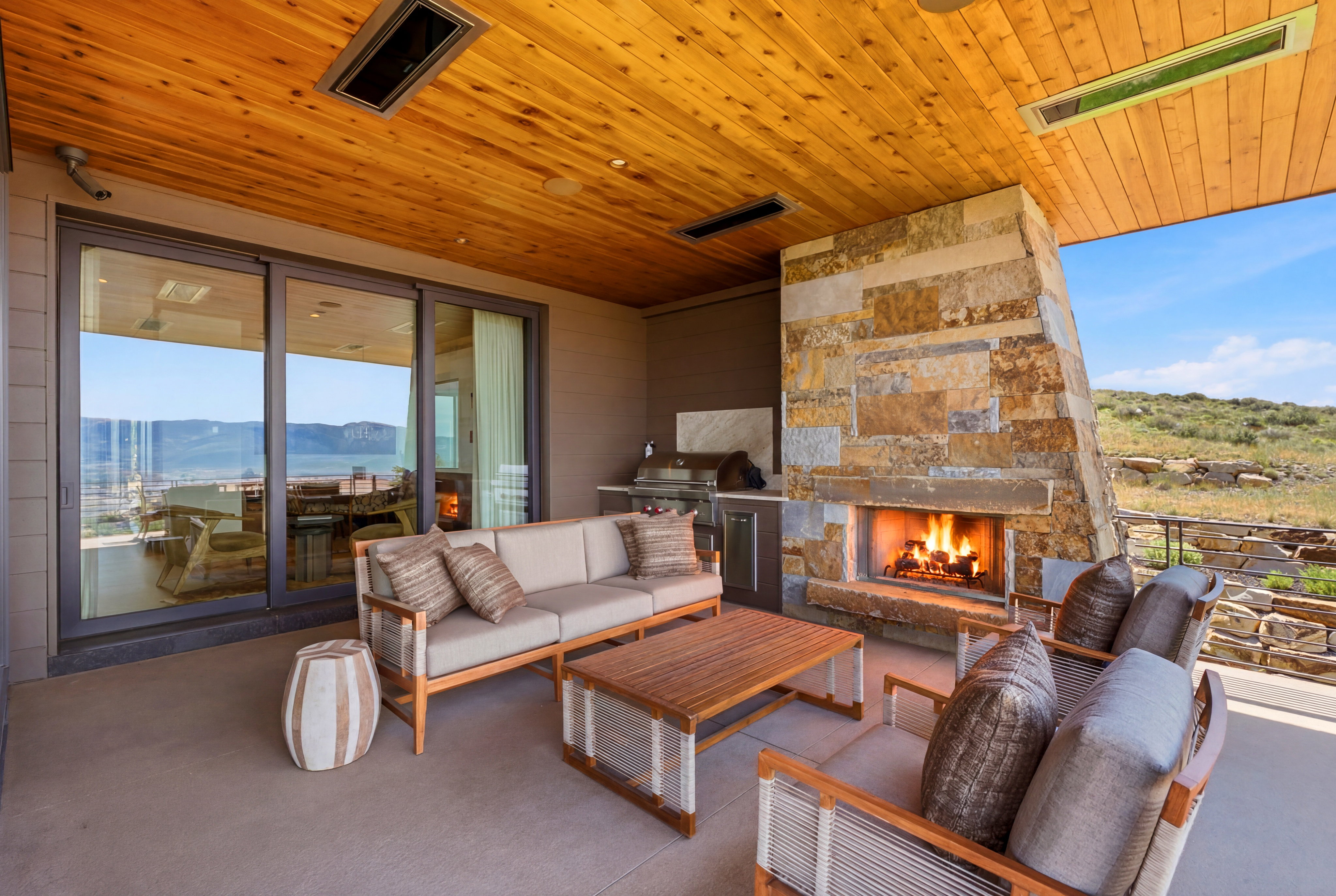 Expansive covered patio featuring a stone-clad fireplace, wood-finish ceiling, and large sliding glass doors