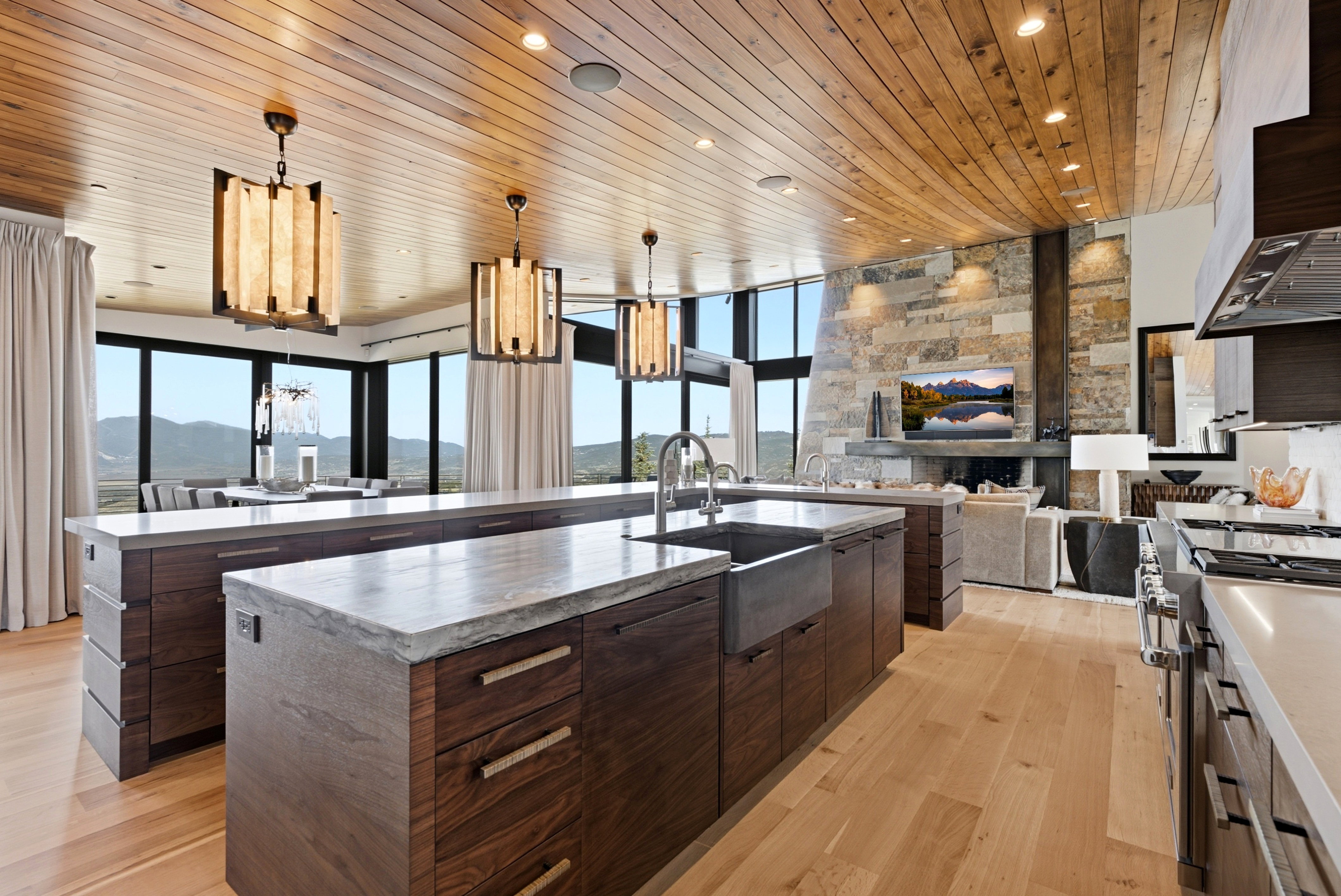 Gourmet kitchen featuring a large farmhouse sink, two expansive islands with stone countertops, integrated stainless steel appliances, and custom wood cabinetry
