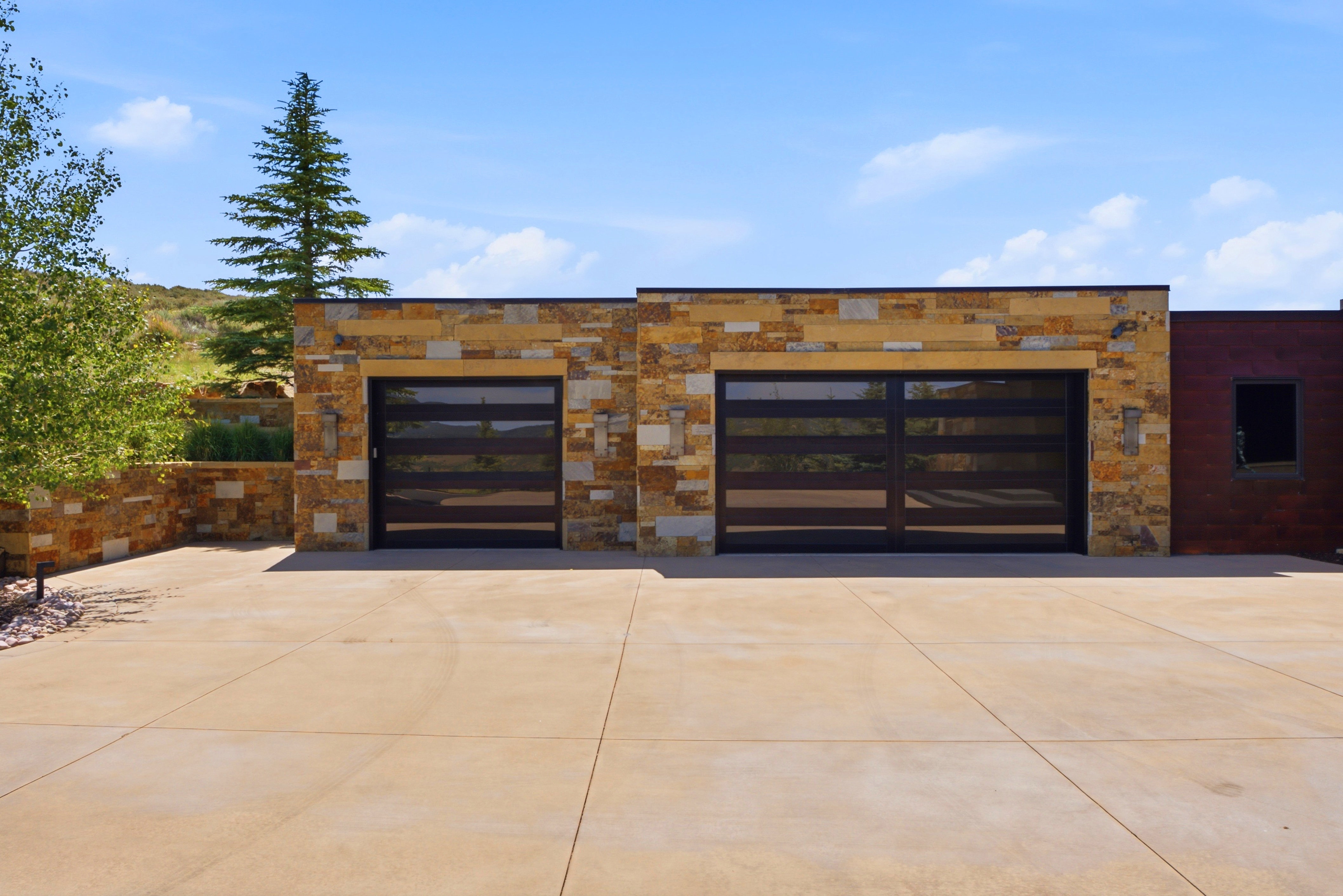Stone veneer facade featuring two dark-framed garage doors with horizontal frosted panels