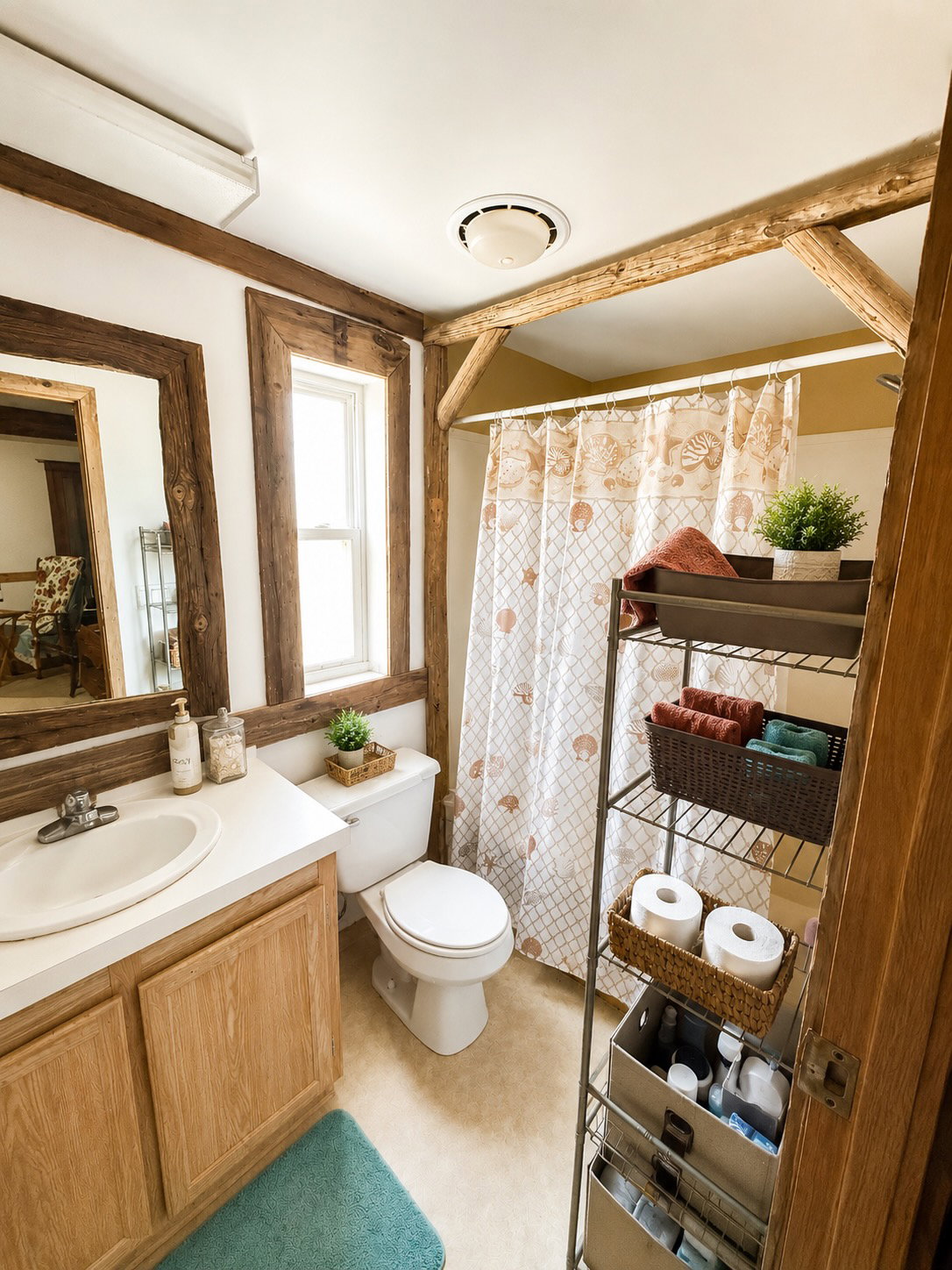 Bathroom featuring exposed timber beams, a window with natural light, a white vanity with a single sink, a toilet, and light-colored flooring