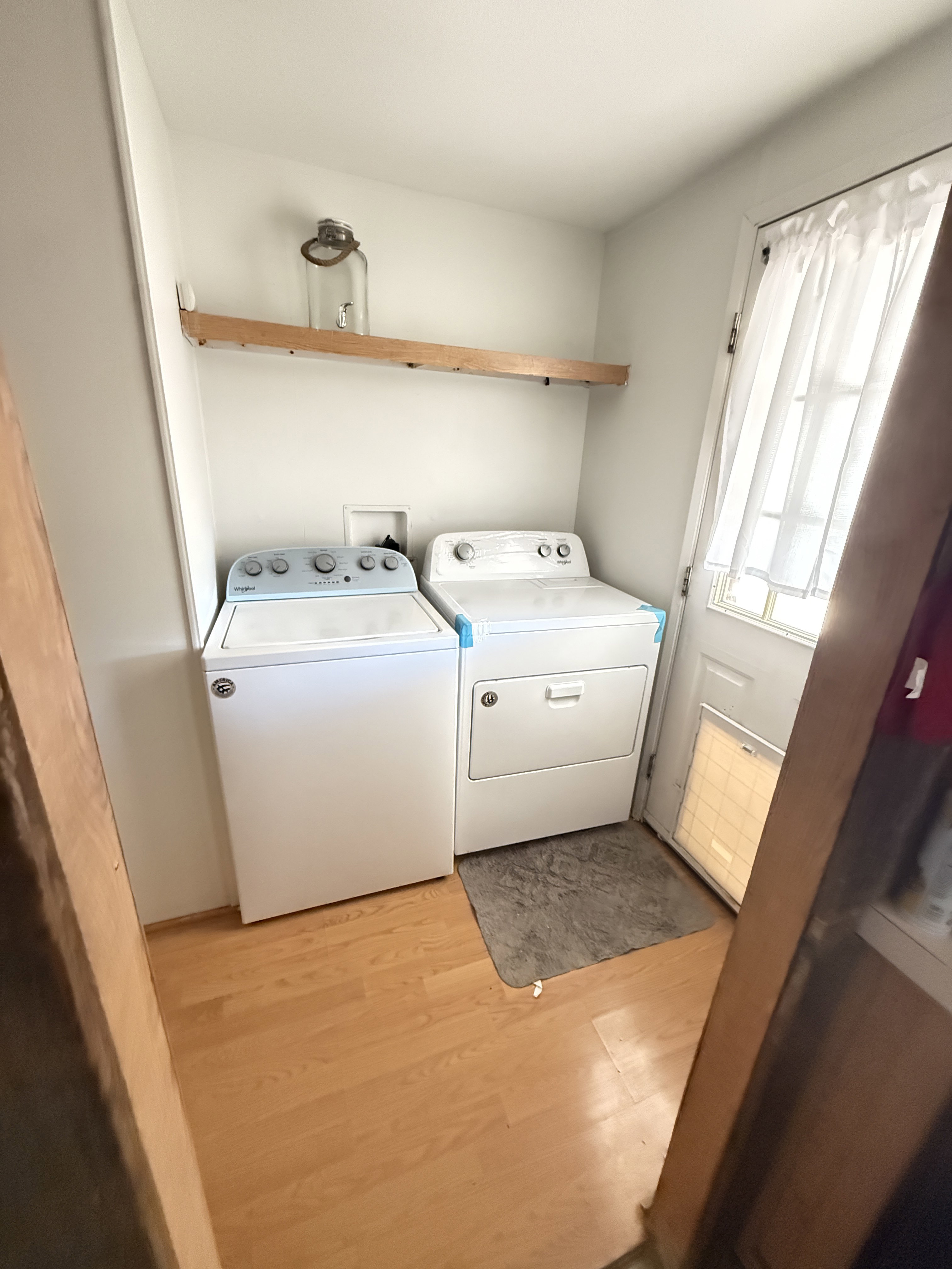 Dedicated laundry area featuring wood-finish flooring, a wall-mounted shelving unit, and a window for natural light
