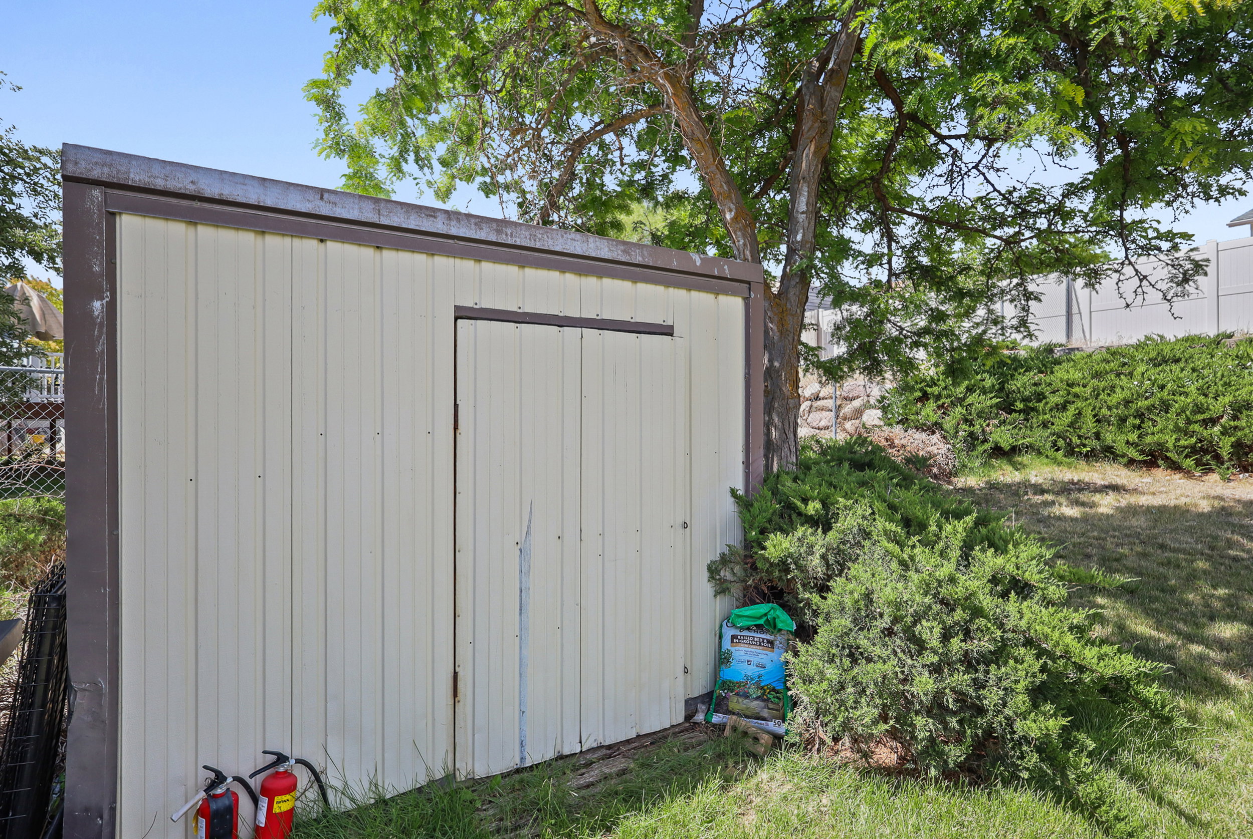 Utility shed with corrugated metal siding, framed by mature trees and shrubs