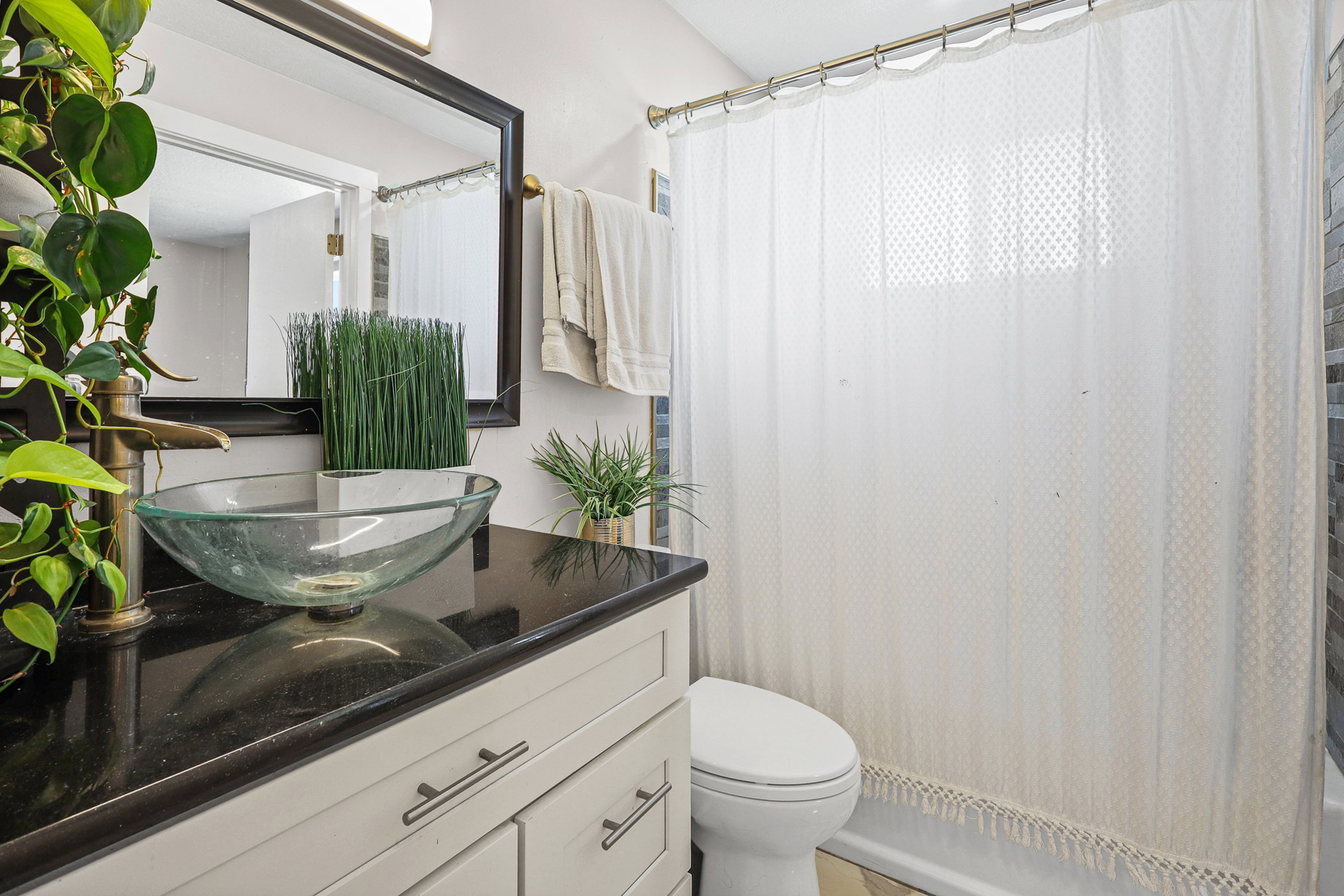 Bathroom vanity featuring a vessel sink, black countertop, light-toned cabinetry, and a framed mirror