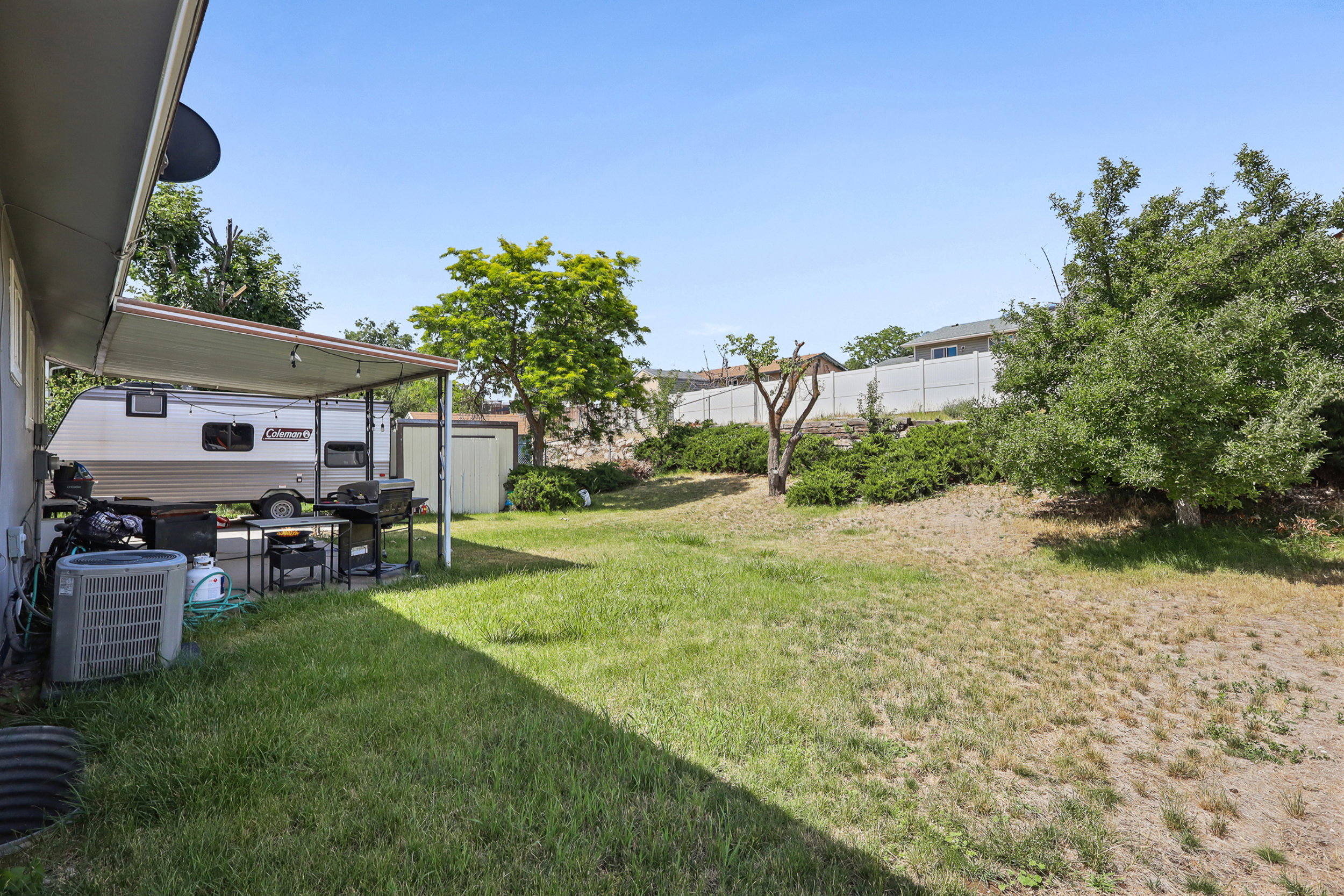 Expansive grass yard with a sloped landscape and mature trees