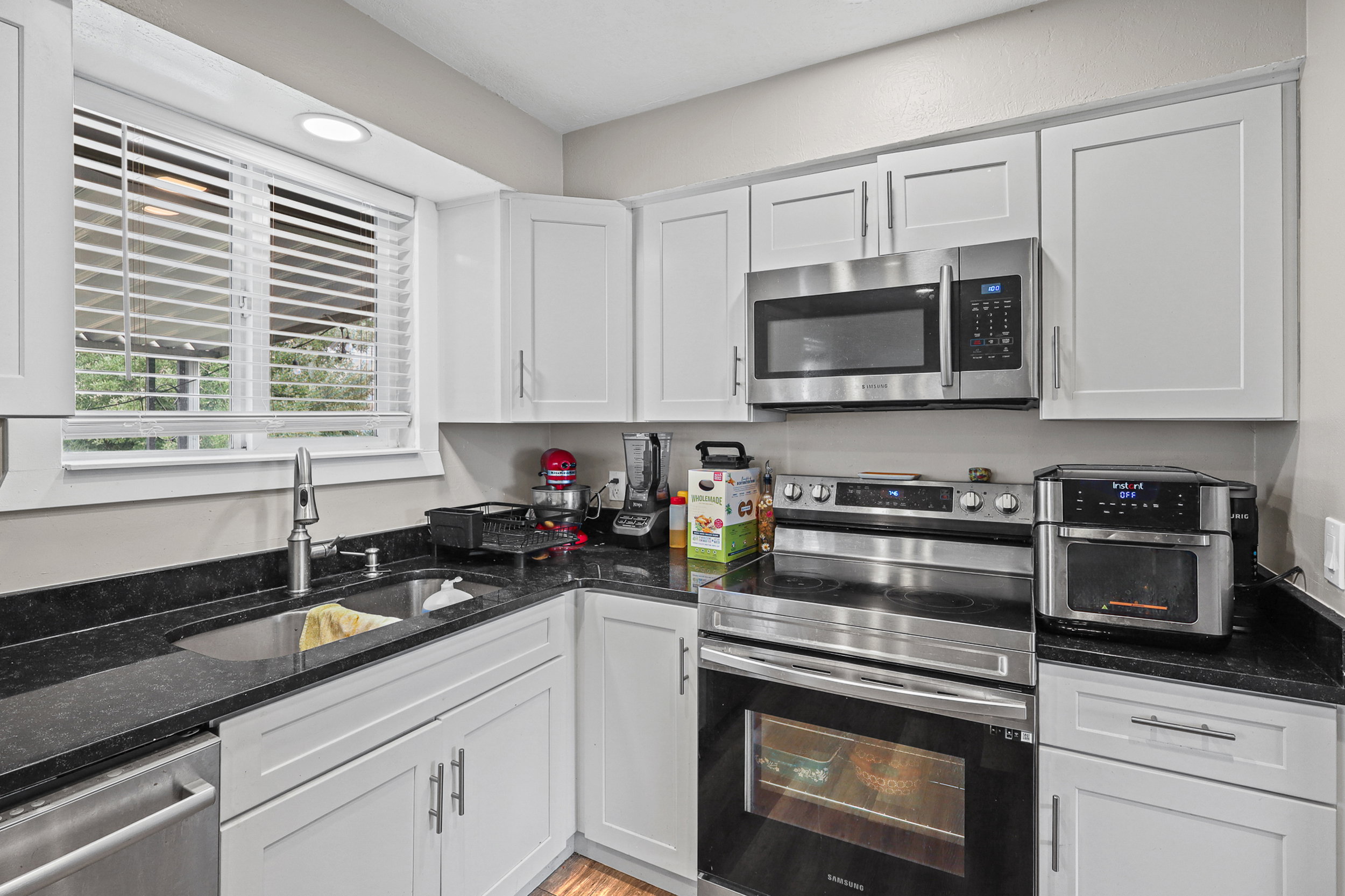 Kitchen featuring white cabinetry, dark speckled countertops, stainless steel appliances, and a window with white blinds