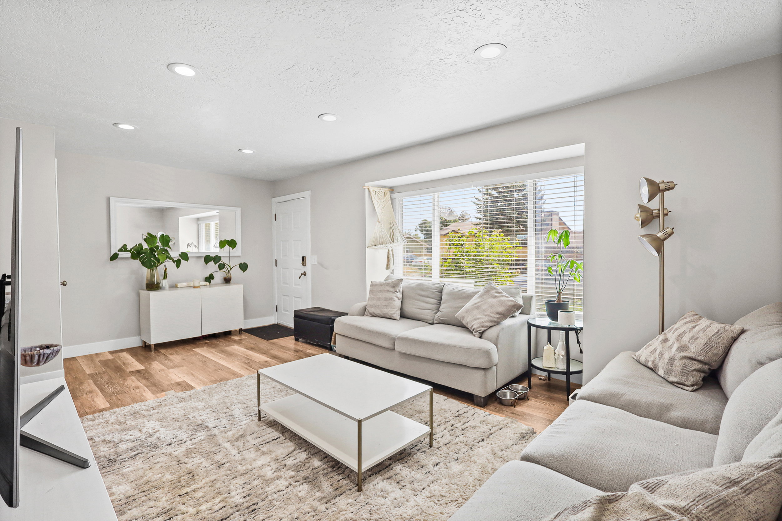 Spacious living area featuring wood-finish flooring, recessed lighting, and a large bay window with blinds