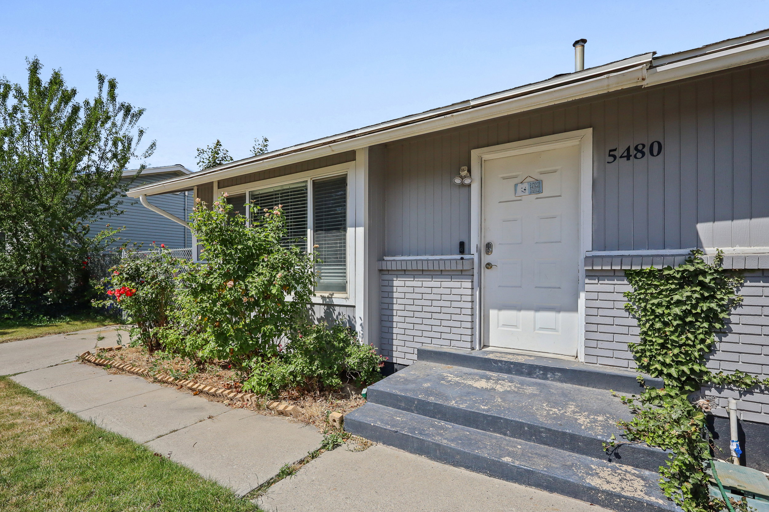 Gray exterior with white trim, featuring a white paneled entry door and a brick facade accent