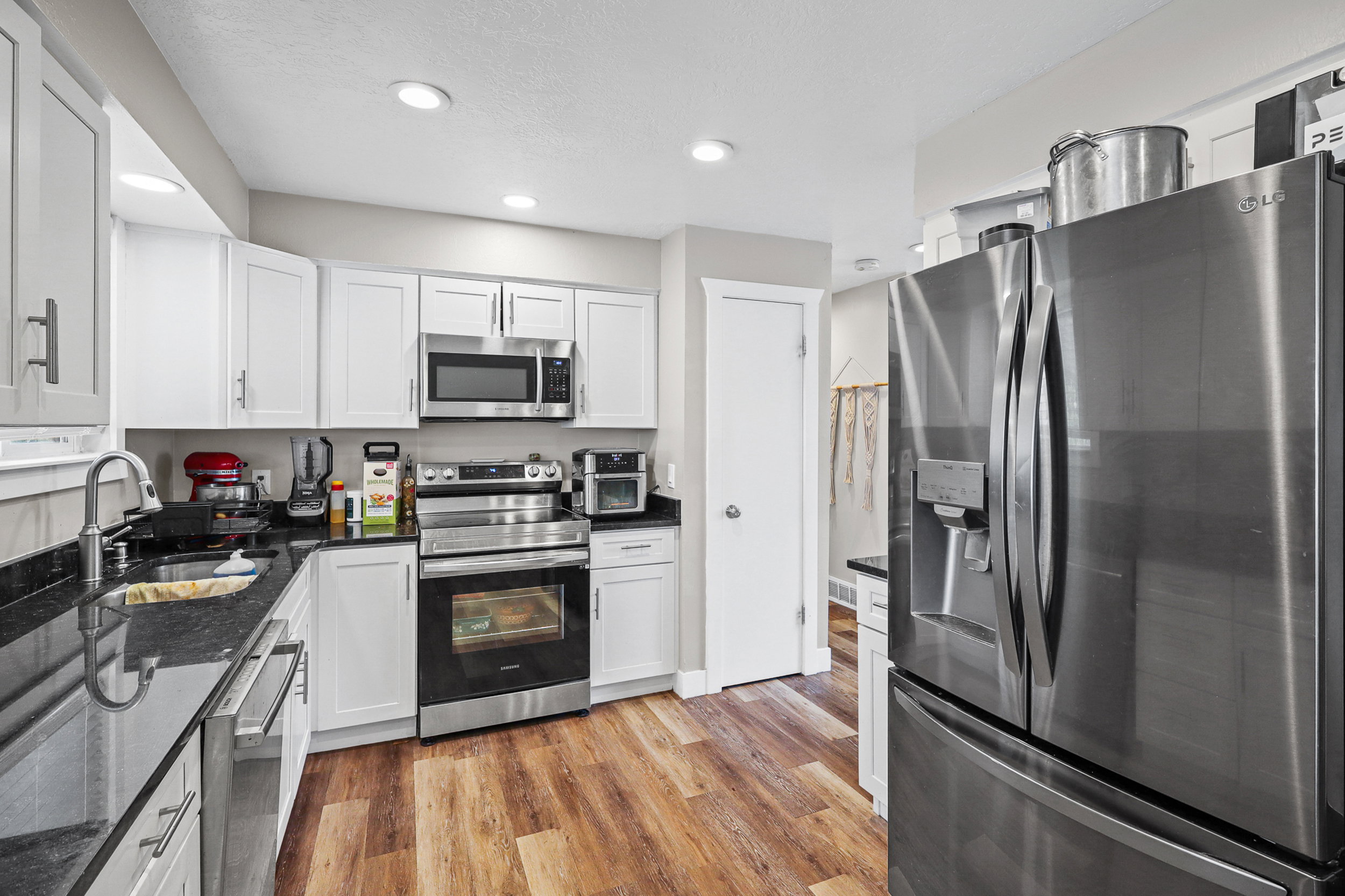 U-shaped kitchen featuring white cabinetry, dark countertops, stainless steel appliances, and wood-finish flooring