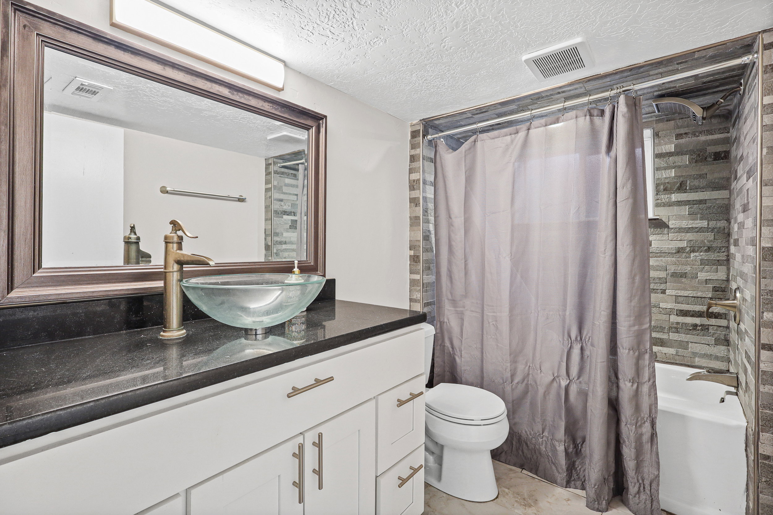 Bathroom featuring a contemporary vessel sink with a bronze-finish faucet, set on a dark countertop