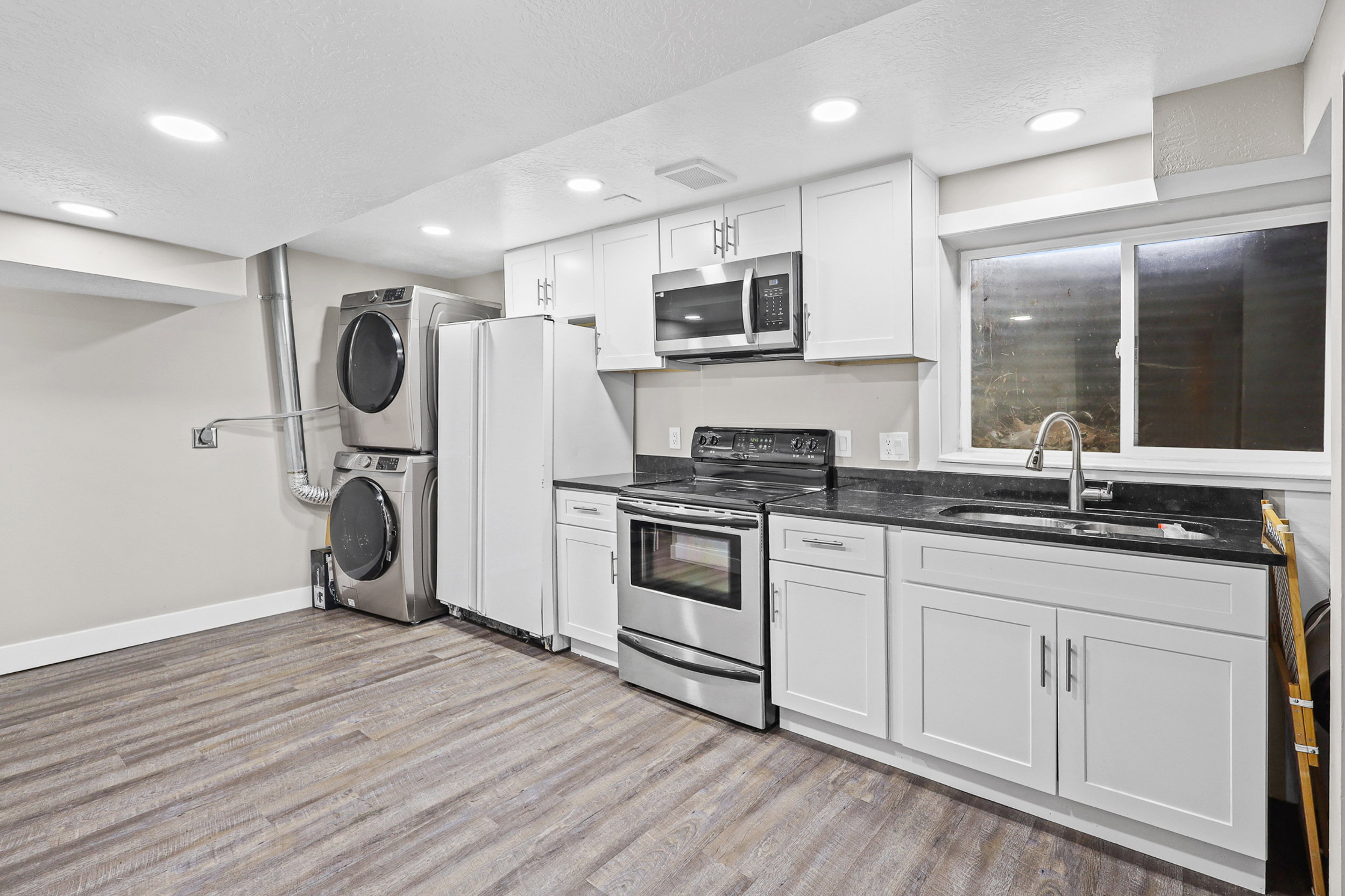 Modern kitchen space featuring white shaker cabinetry, dark granite-style countertops, and stainless steel appliances