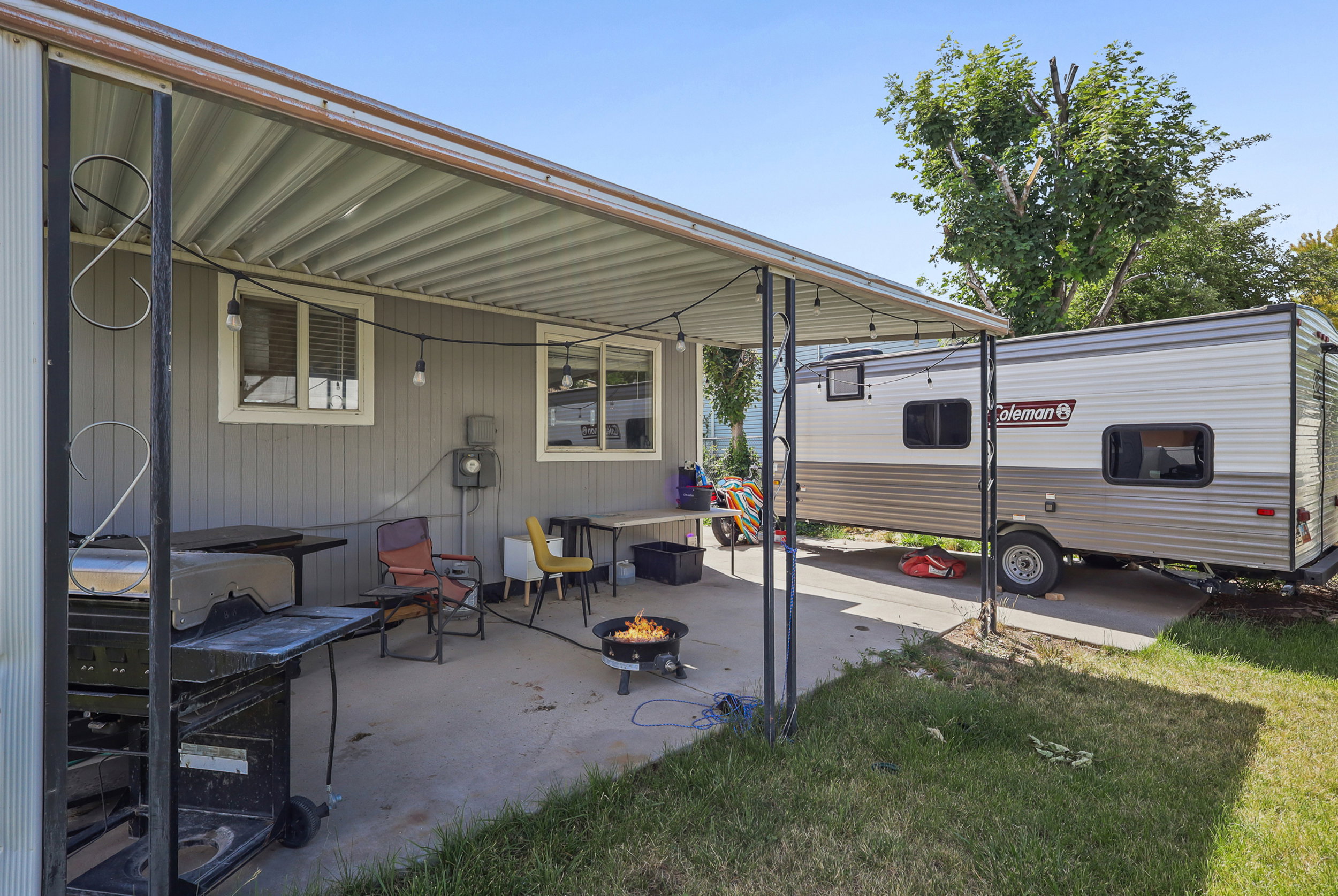 Patio area featuring a corrugated metal awning, string lighting, and direct access to the main structure with vertical siding and multiple windows