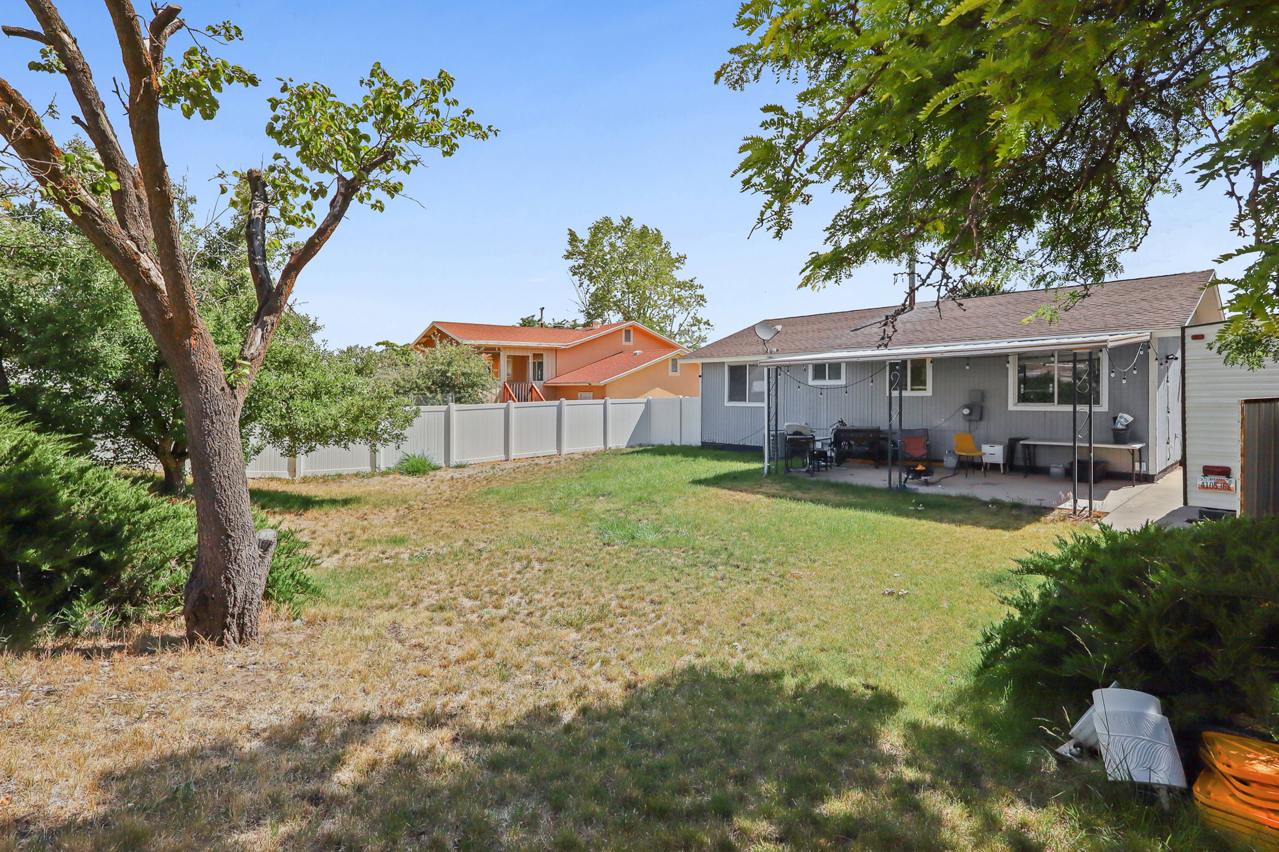 Expansive backyard featuring a partial lawn, mature trees, and a covered patio