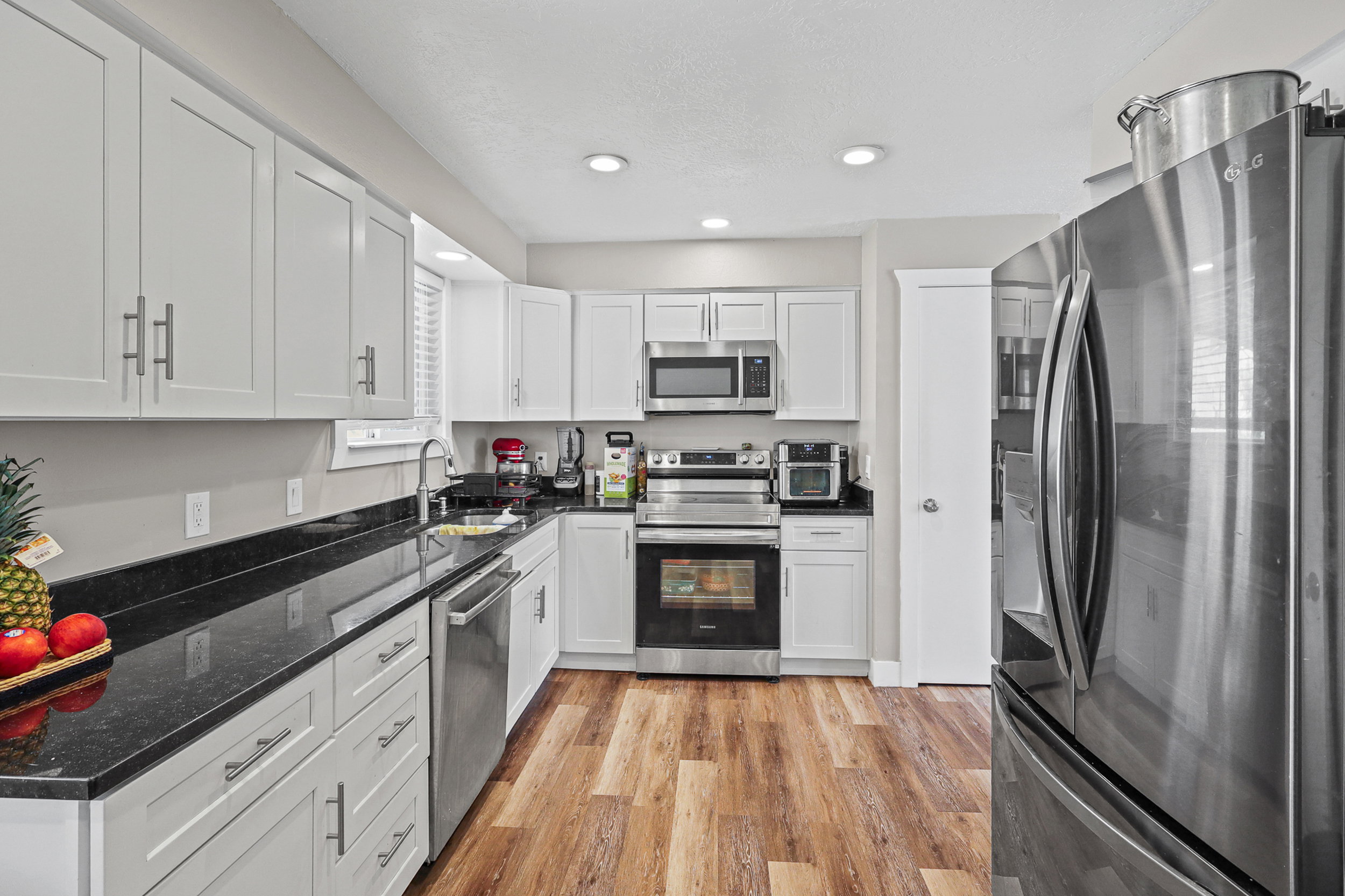 Contemporary kitchen featuring white cabinetry, dark countertops, stainless steel appliances, wood-finish flooring, and recessed lighting