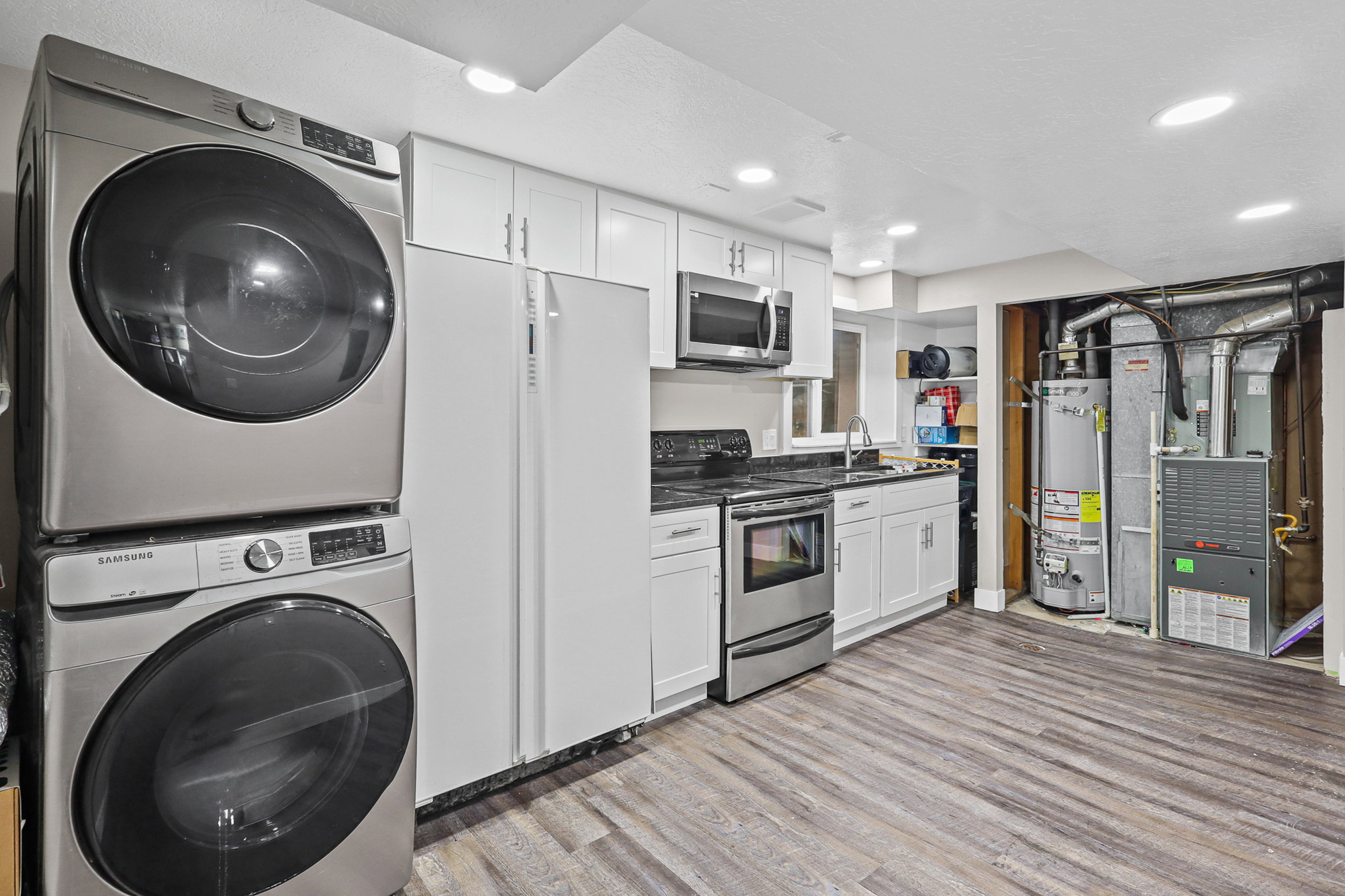 Full kitchen area featuring white cabinetry, stainless steel appliances, dark countertops, and wood-finish flooring