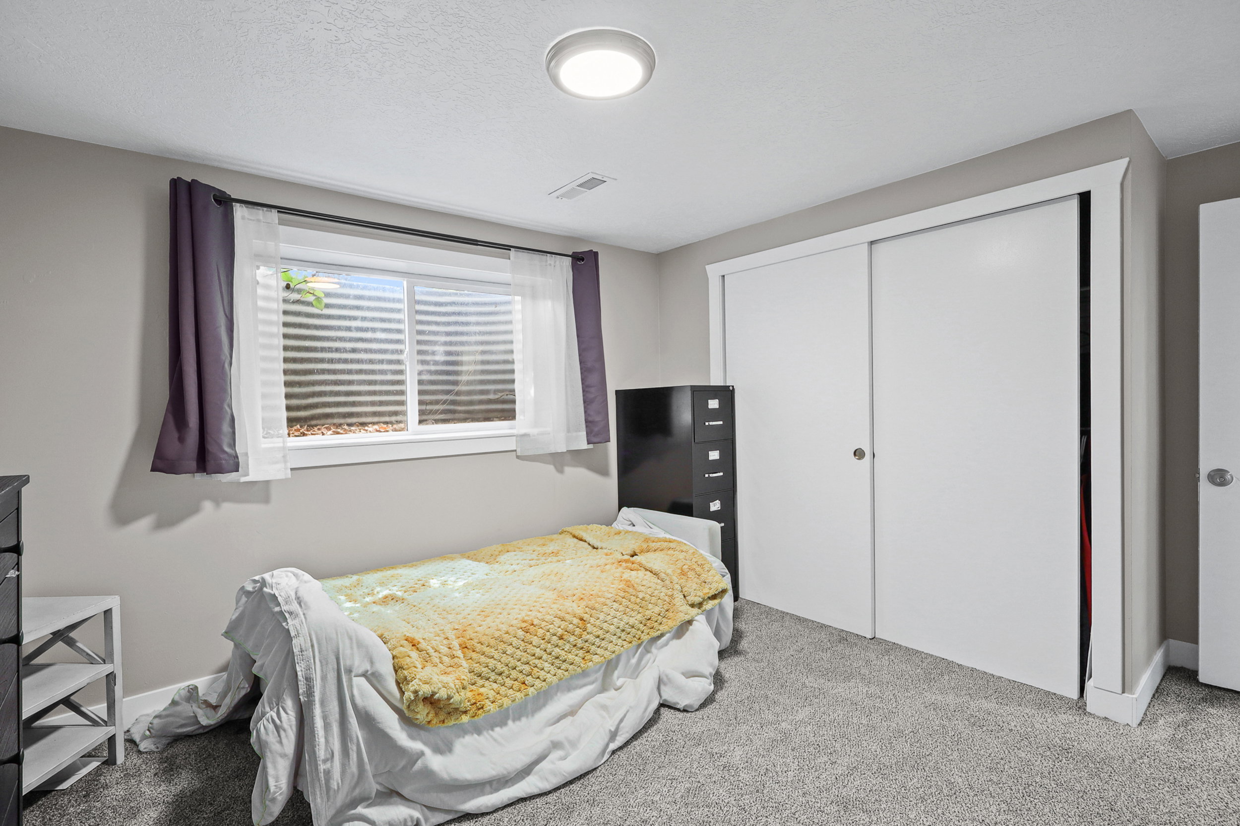 Carpeted room featuring a window with white trim, a flush-mount ceiling light, and white sliding closet doors