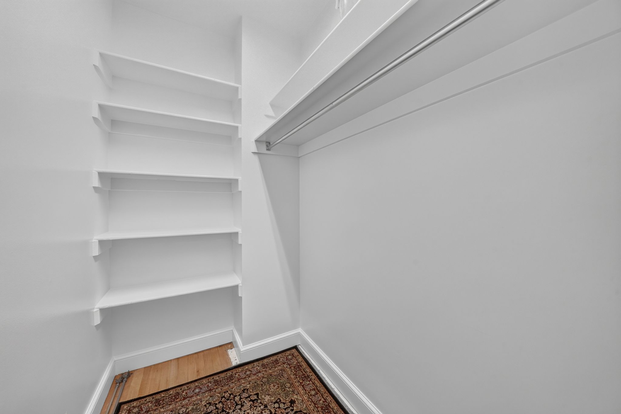 Walk-in closet featuring extensive built-in shelving, a garment rod, light wood-finish flooring, and white baseboards