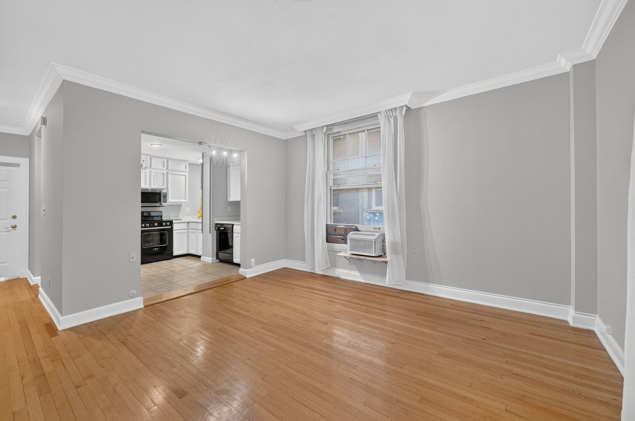 Hardwood flooring in a spacious room featuring crown molding and light gray walls