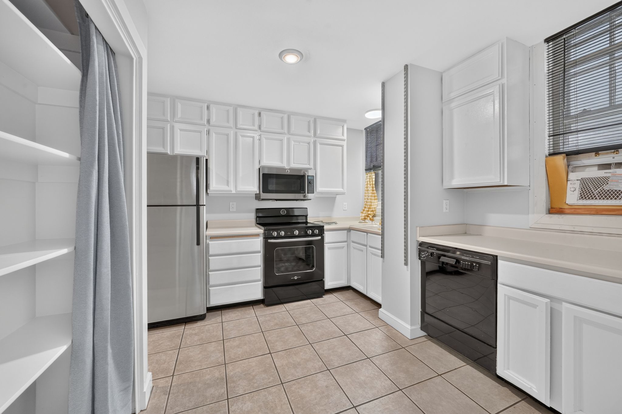Kitchen featuring white cabinetry, tile flooring, light-toned countertops, stainless steel refrigerator, and built-in microwave