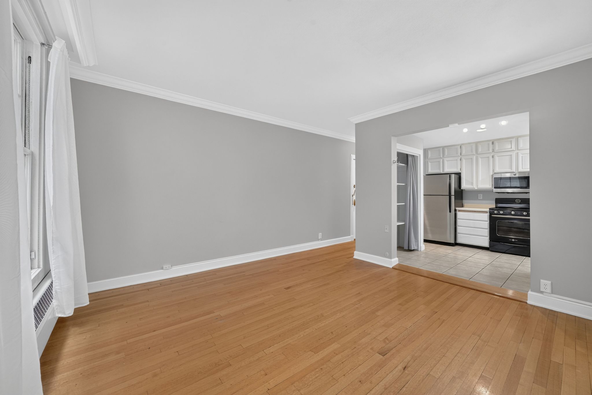 Hardwood flooring extending through the main living area, complemented by crown molding and a window with a radiator below