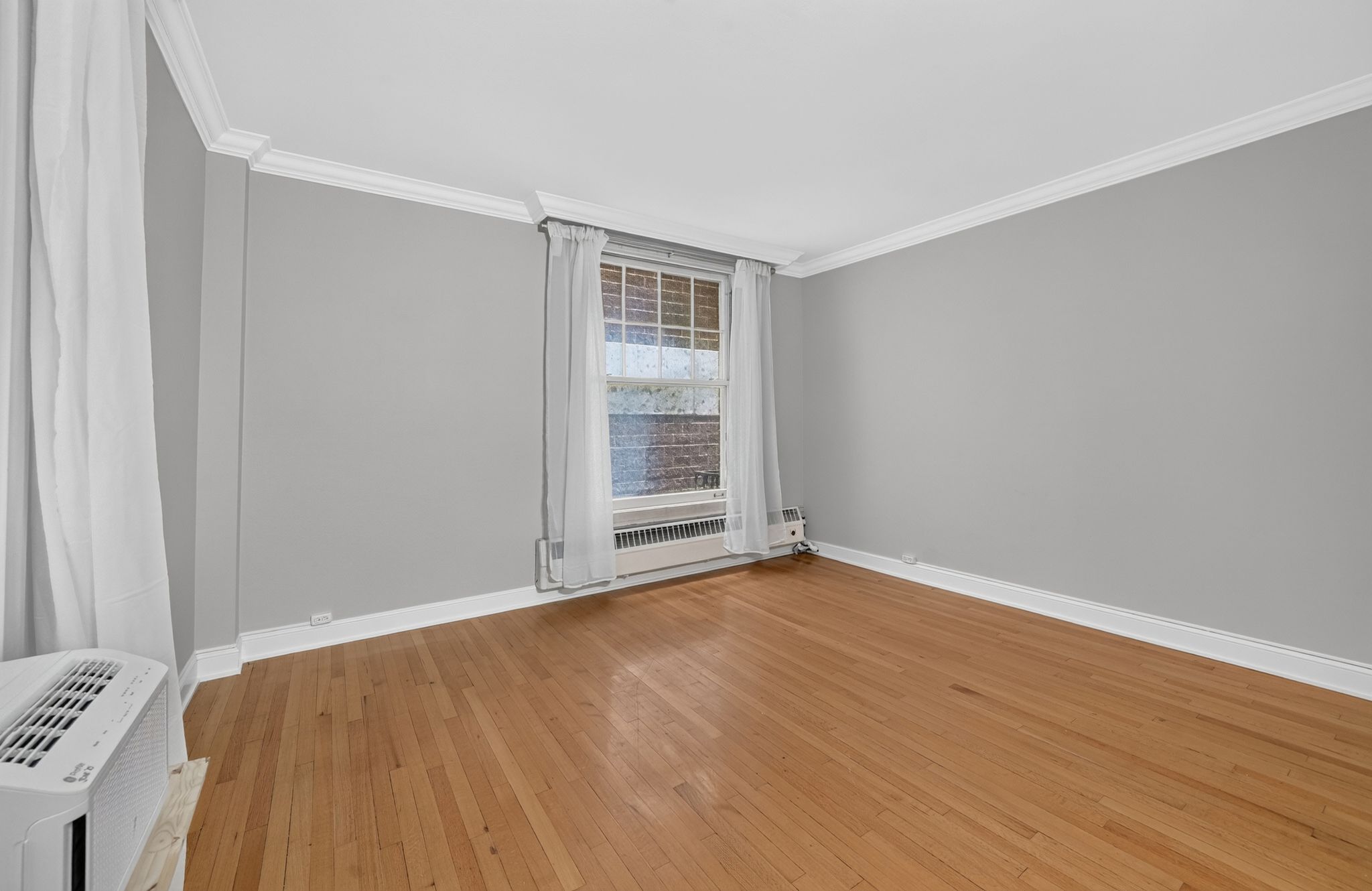 Hardwood flooring extending throughout, complemented by a window providing natural light, crown molding, and white baseboards
