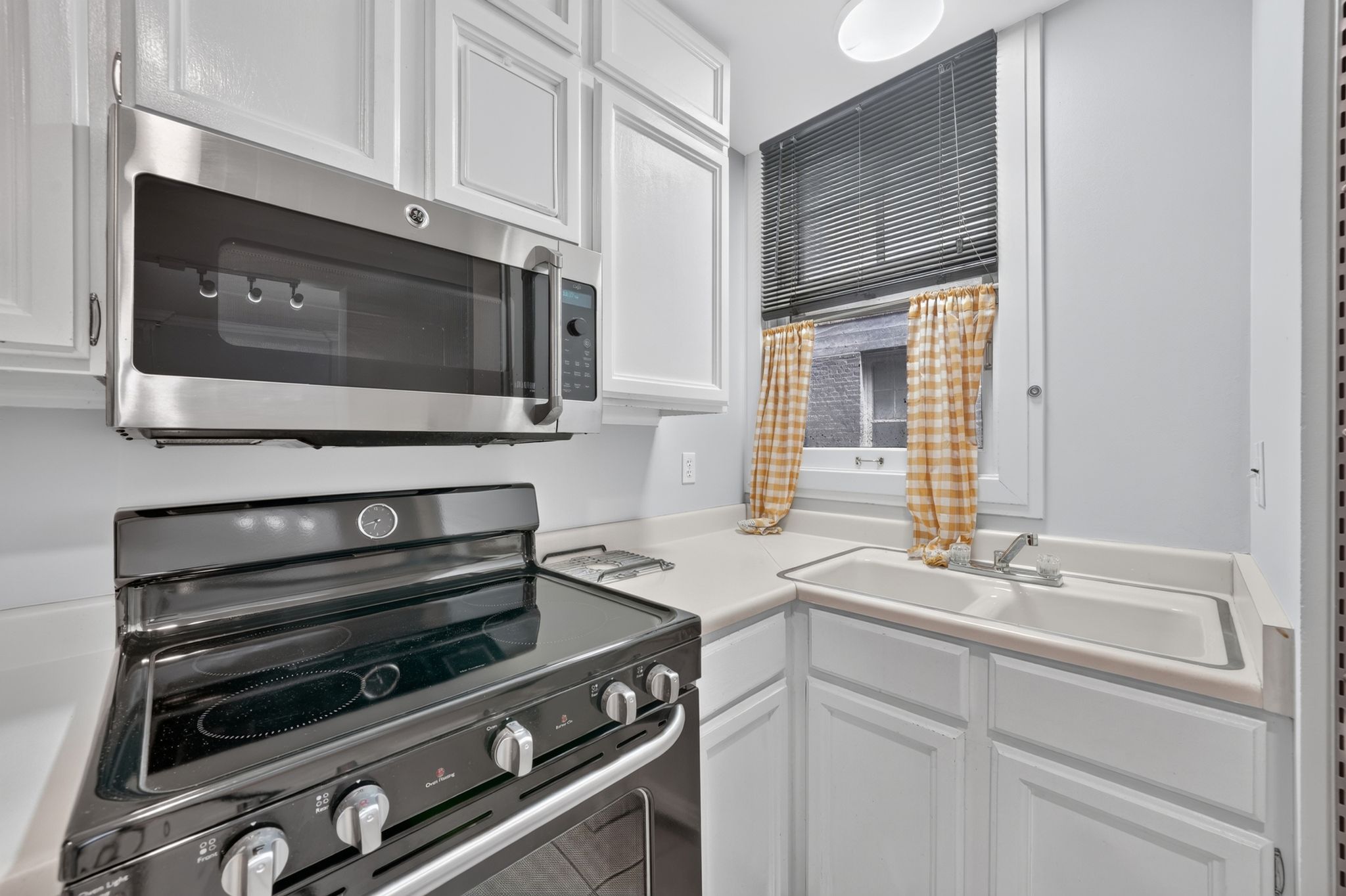 Kitchen featuring white cabinetry, stainless steel over-the-range microwave, black electric range, and light-toned countertops