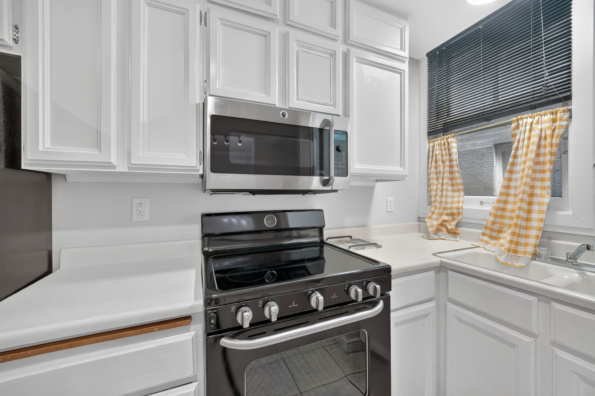 Updated kitchen featuring white shaker cabinetry, white countertops, stainless steel microwave, black range, and a white sink with a chrome faucet
