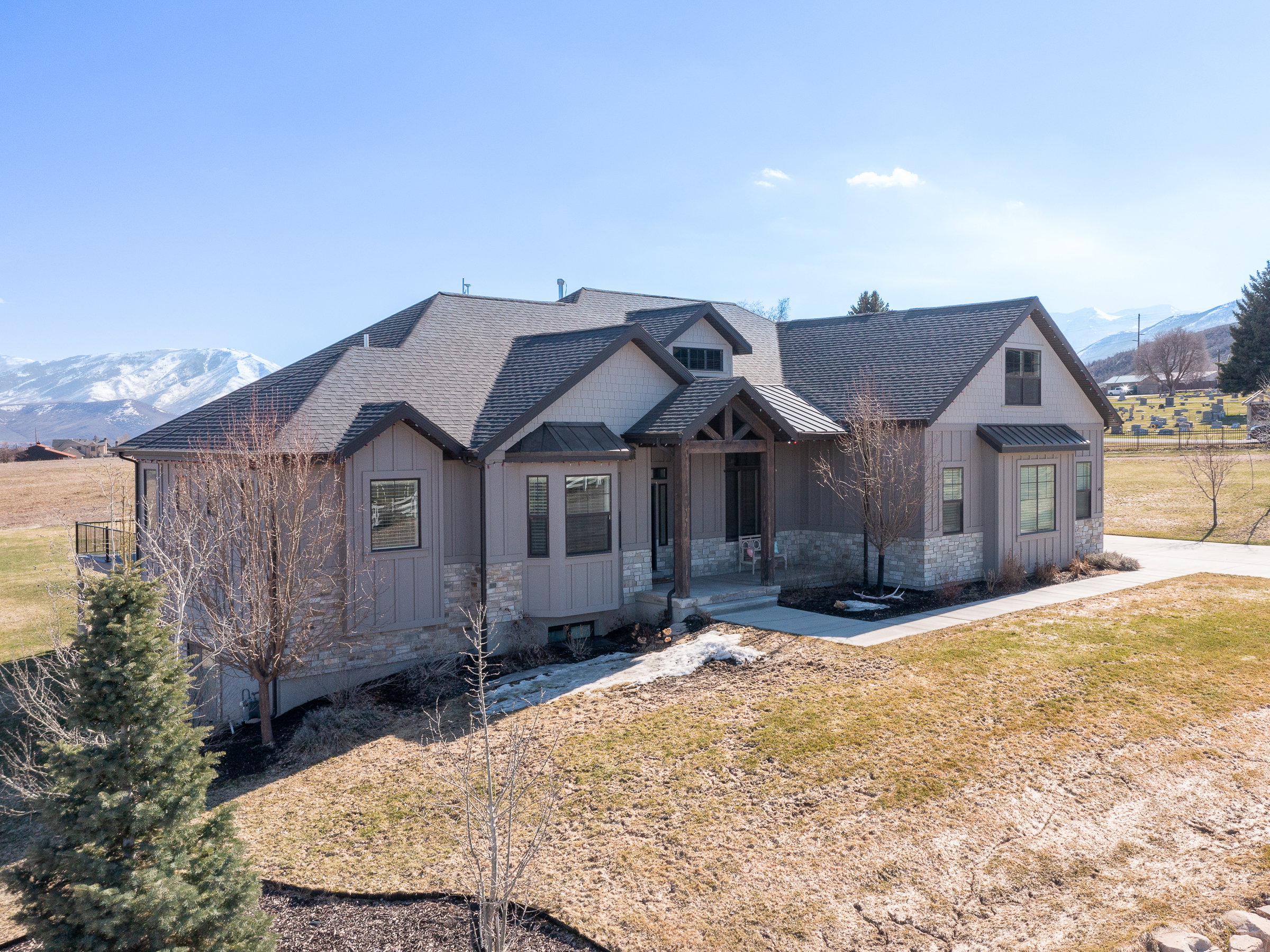 Contemporary residence featuring a covered entry, stone and vertical siding exterior, black-framed windows, a dark shingle roof, and a concrete driveway