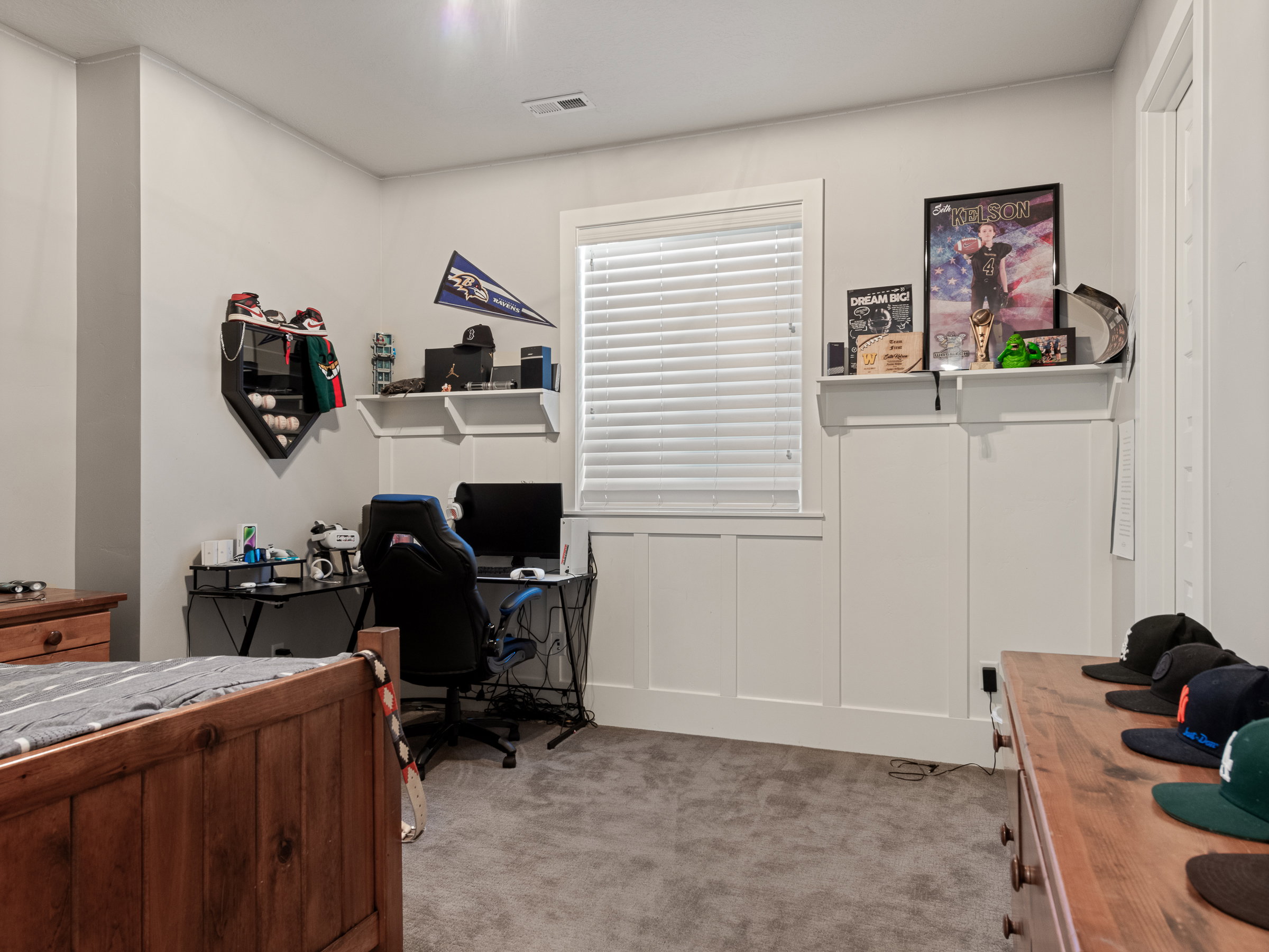 Carpeted room featuring a single window with blinds, white board and batten paneling, built-in shelving, and light gray painted walls